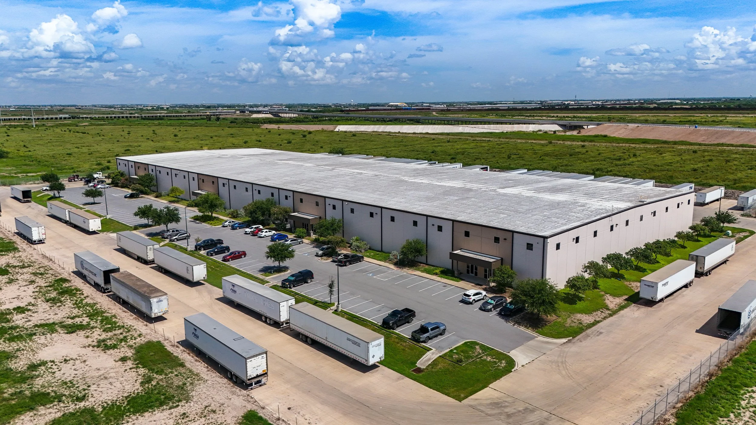 Large warehouse building with surrounding parking lot and multiple trucks parked along the driveway