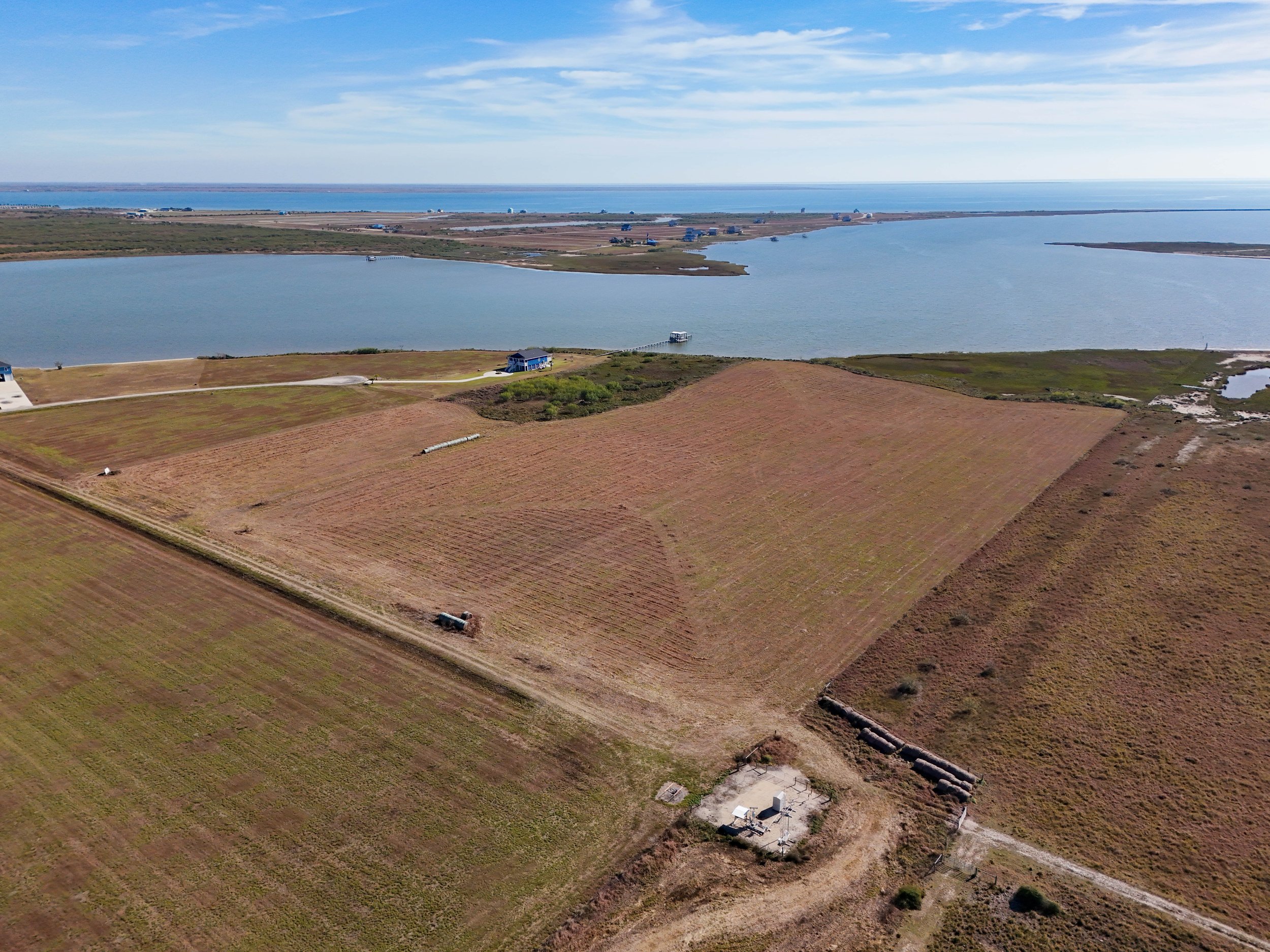 Aerial view of farmland with multiple fields, some with crops, near a large body of water under a partly cloudy sky.