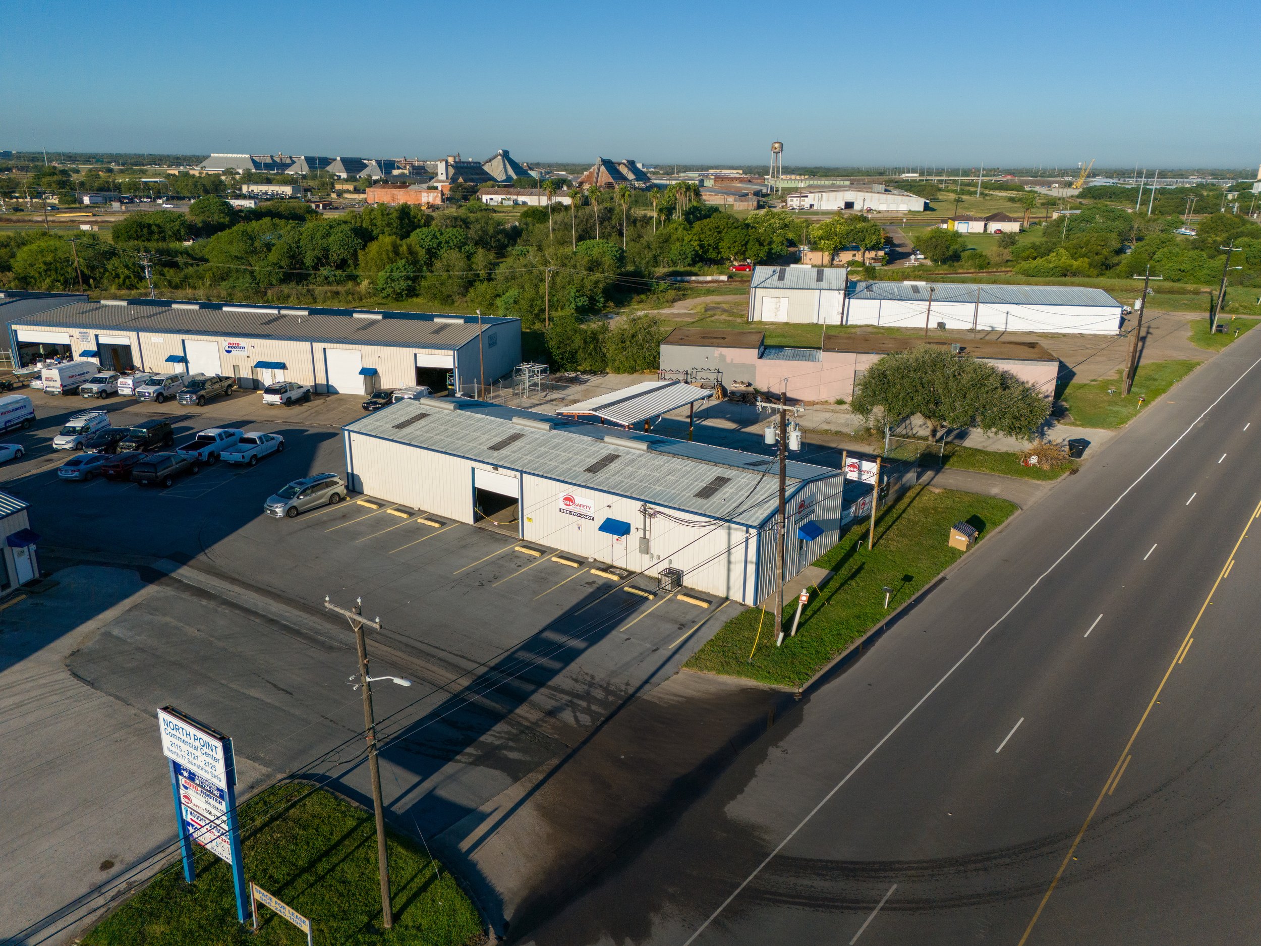 An aerial view of a commercial area with parking lots, industrial buildings, and a main road.
