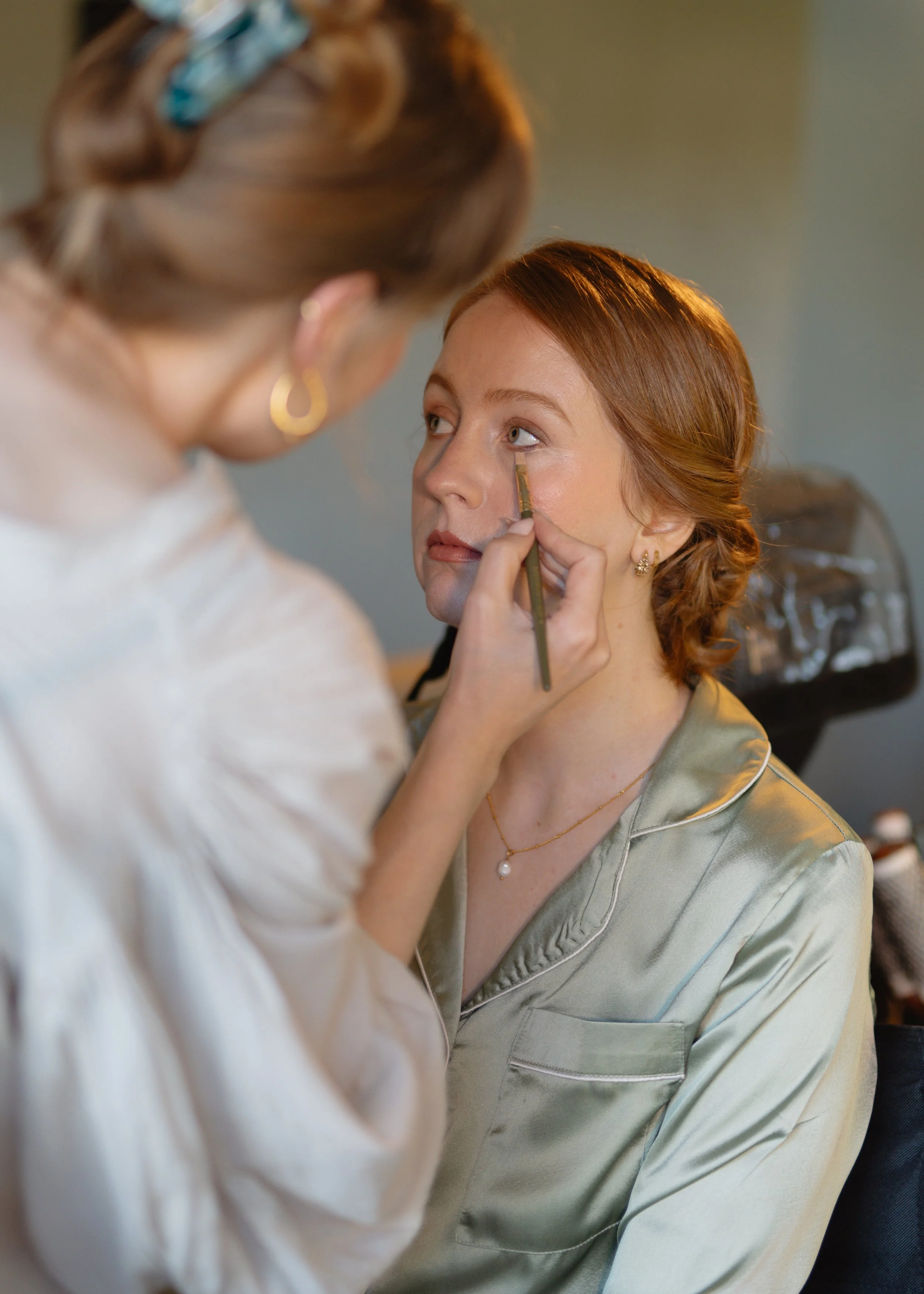 Makeup artist applying makeup to a woman sitting down, with a brush near her eye.
