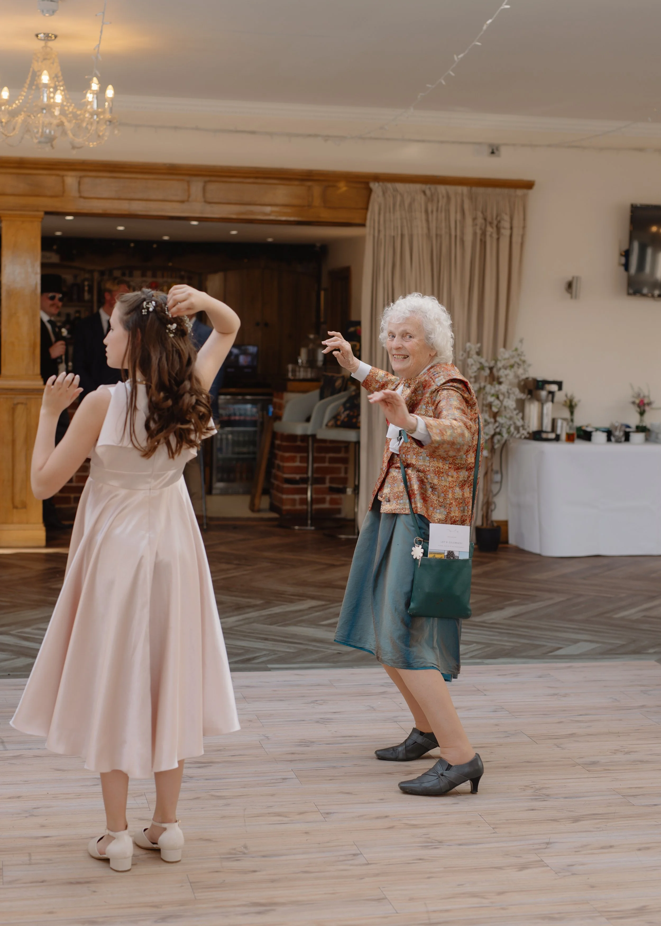 An elderly woman dancing joyfully with a young woman at a celebration event in a decorated indoor venue.