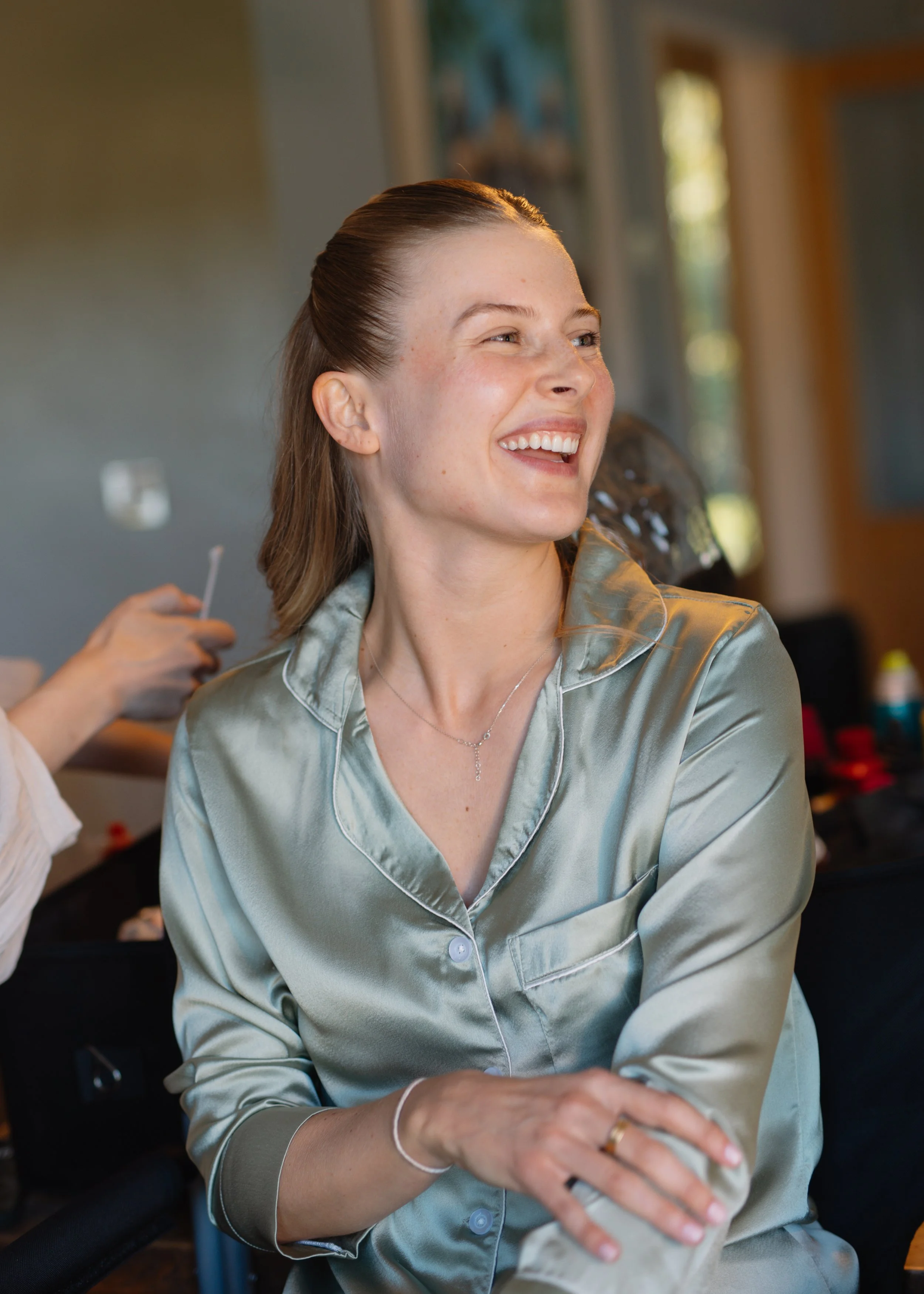 A woman with light skin, brown hair, and a satin button-up shirt, smiling and looking to her right