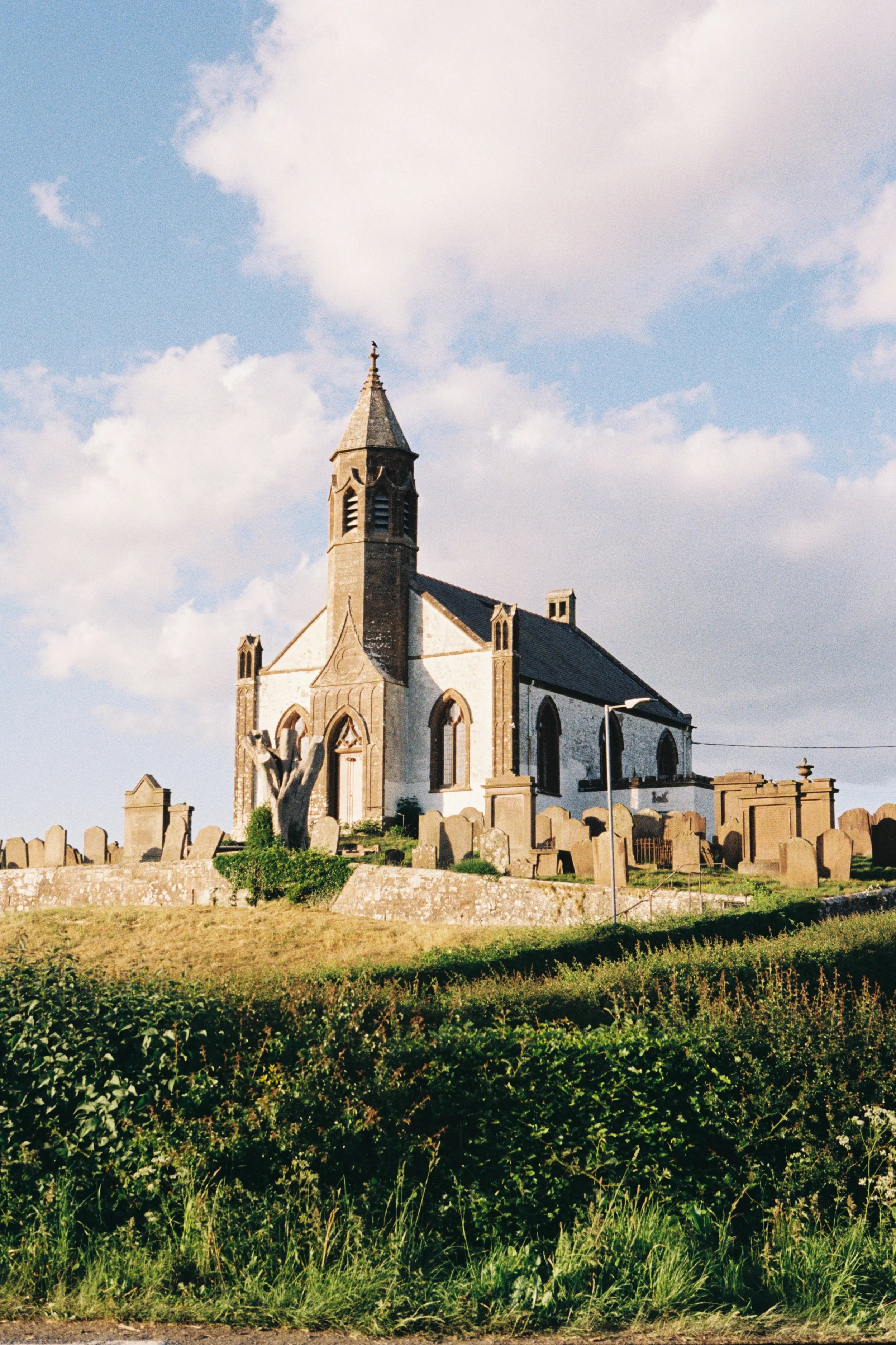 A church with a tall steeple and graveyard in the foreground, under a partly cloudy sky.