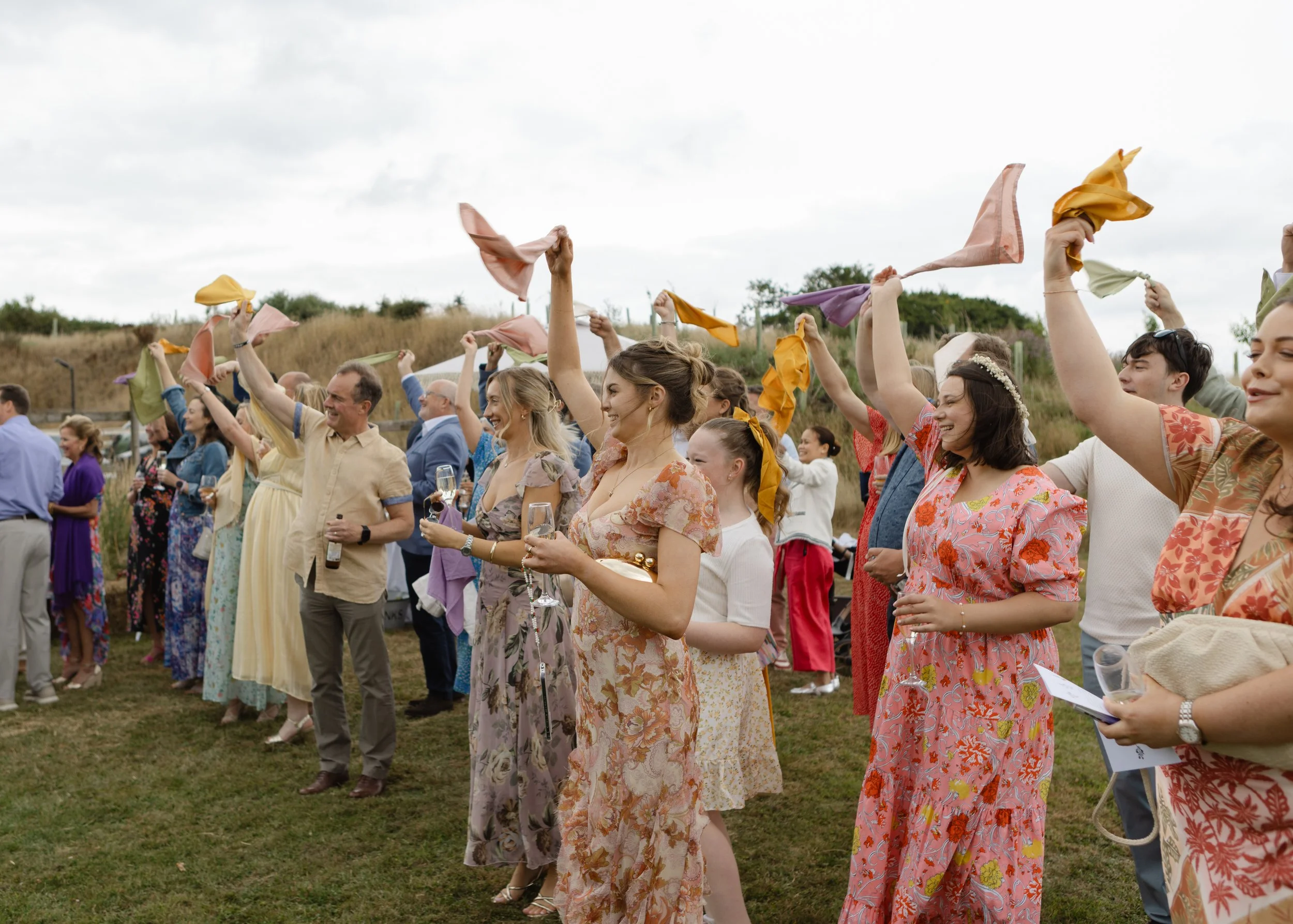 People holding colorful cloths and glasses of wine at an outdoor celebration, smiling and enjoying the event.
