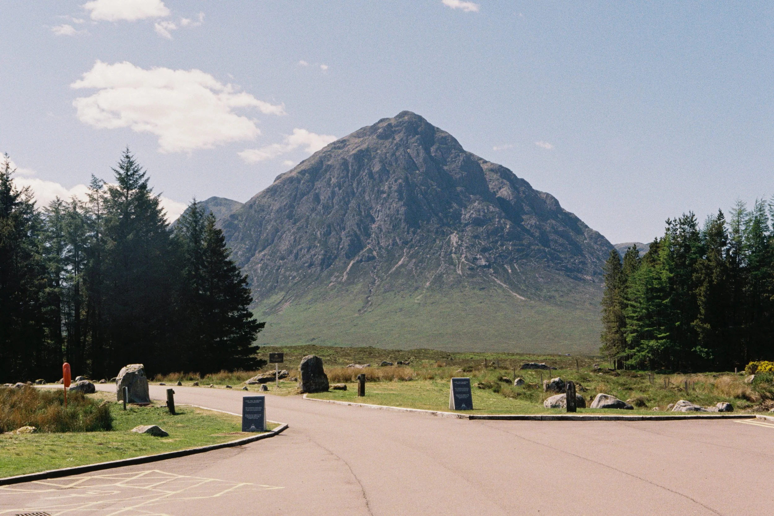 Mountains in the background with a forested area and a paved parking lot in the foreground.