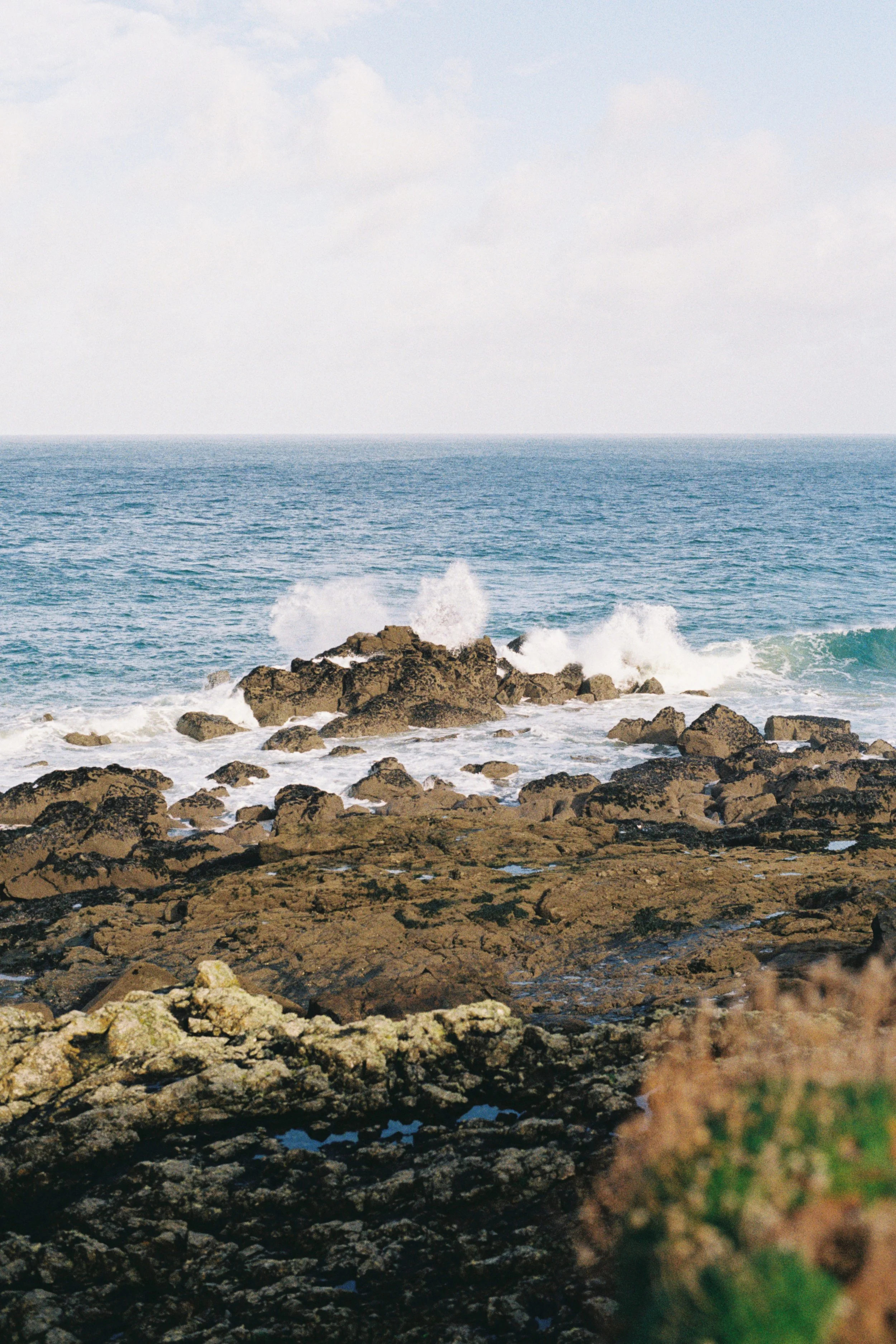 Rocky shoreline with ocean waves crashing against rocks under a cloudy sky