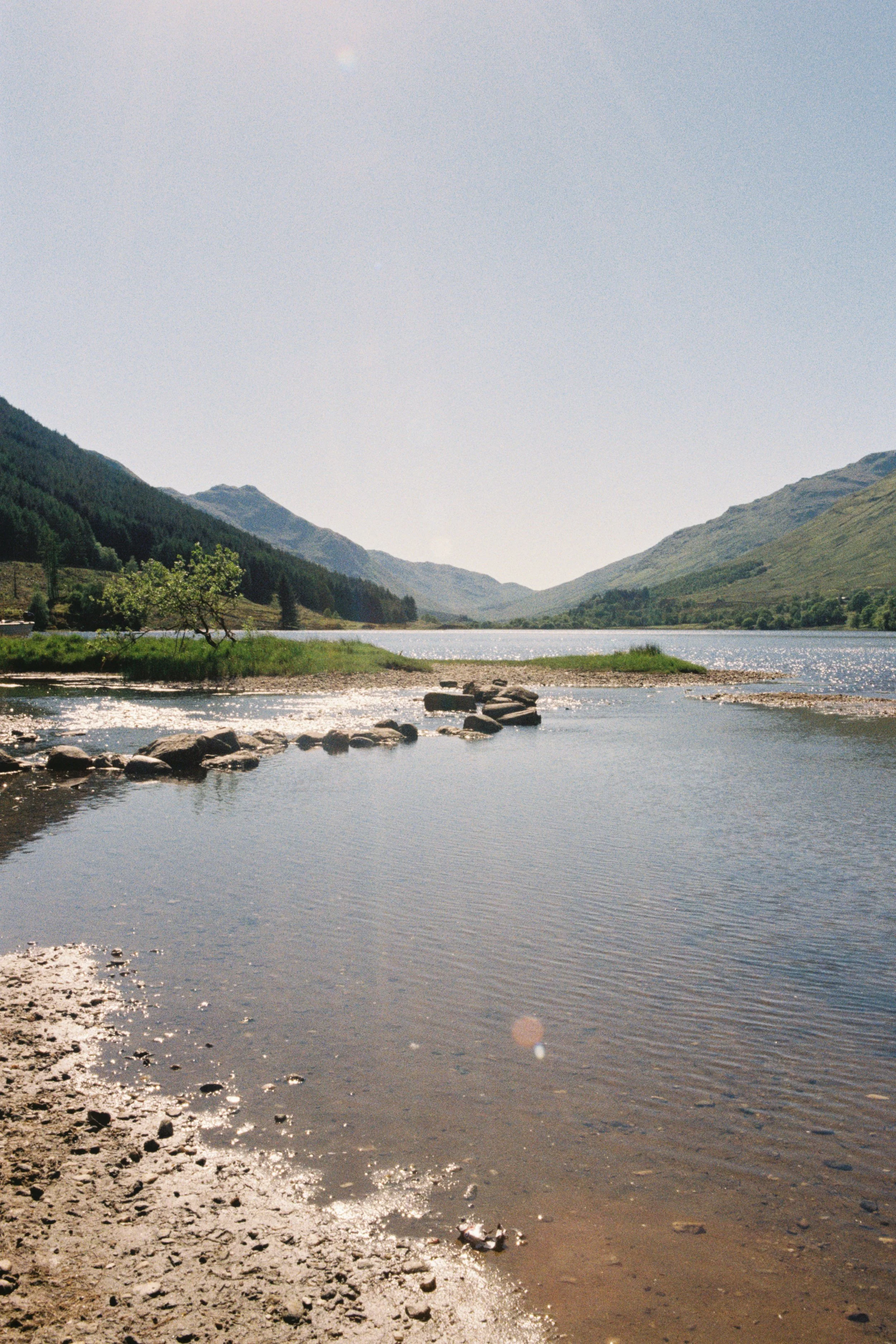 A river flowing through a valley surrounded by green mountains on a sunny day.