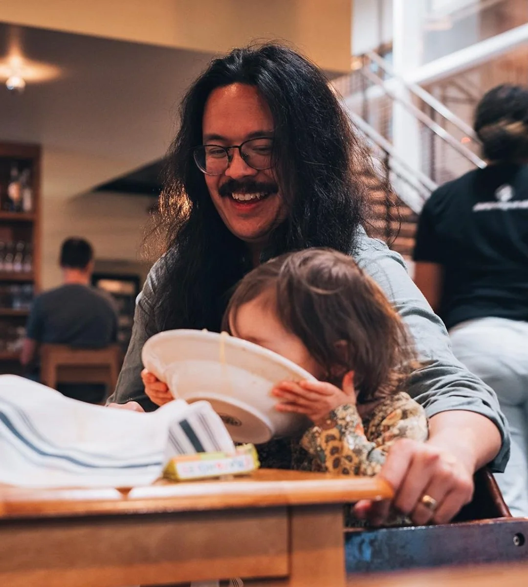 Parent and child at a restaurant, the child drinking from a pasta bowl.