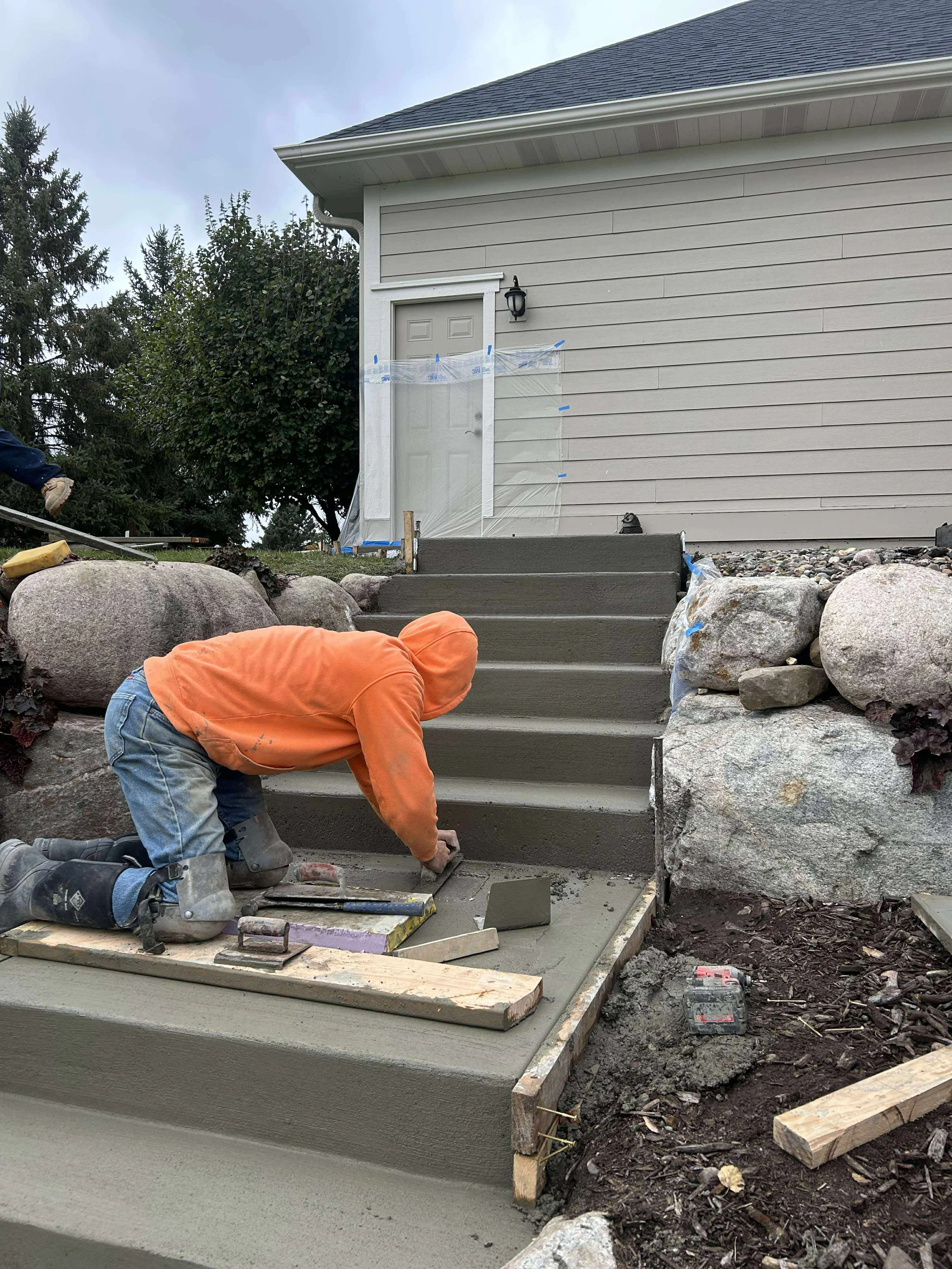 A scenic landscape featuring a large body of turquoise water with rolling grassy hills in the foreground and rugged mountain ranges in the background under a cloudy sky.