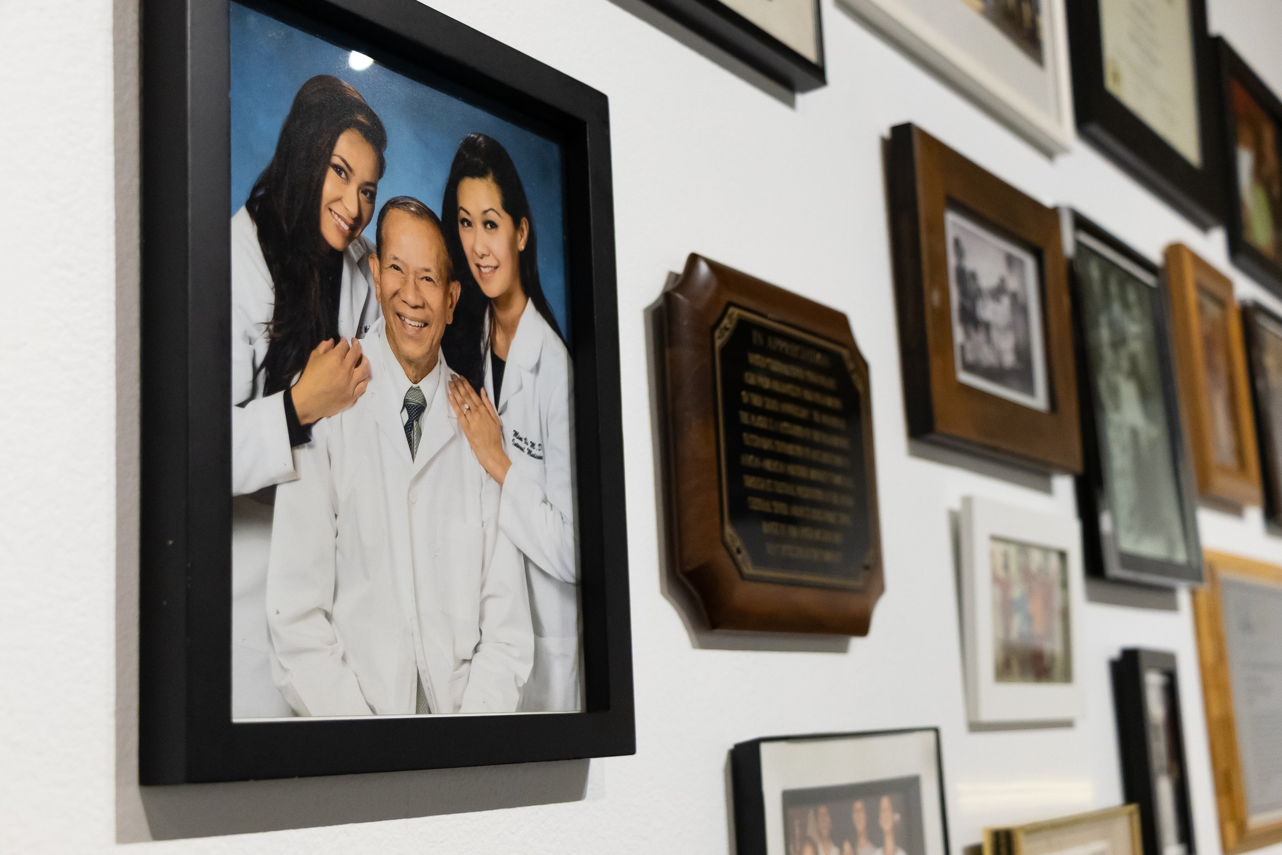 Awards and Photos: This wall features awards as well as photos of those who have supported everyone on their journeys. The photo here shows Dr. Thanh Vo, who started his medical career all over again after fleeing Vietnam, with his daughters who also
