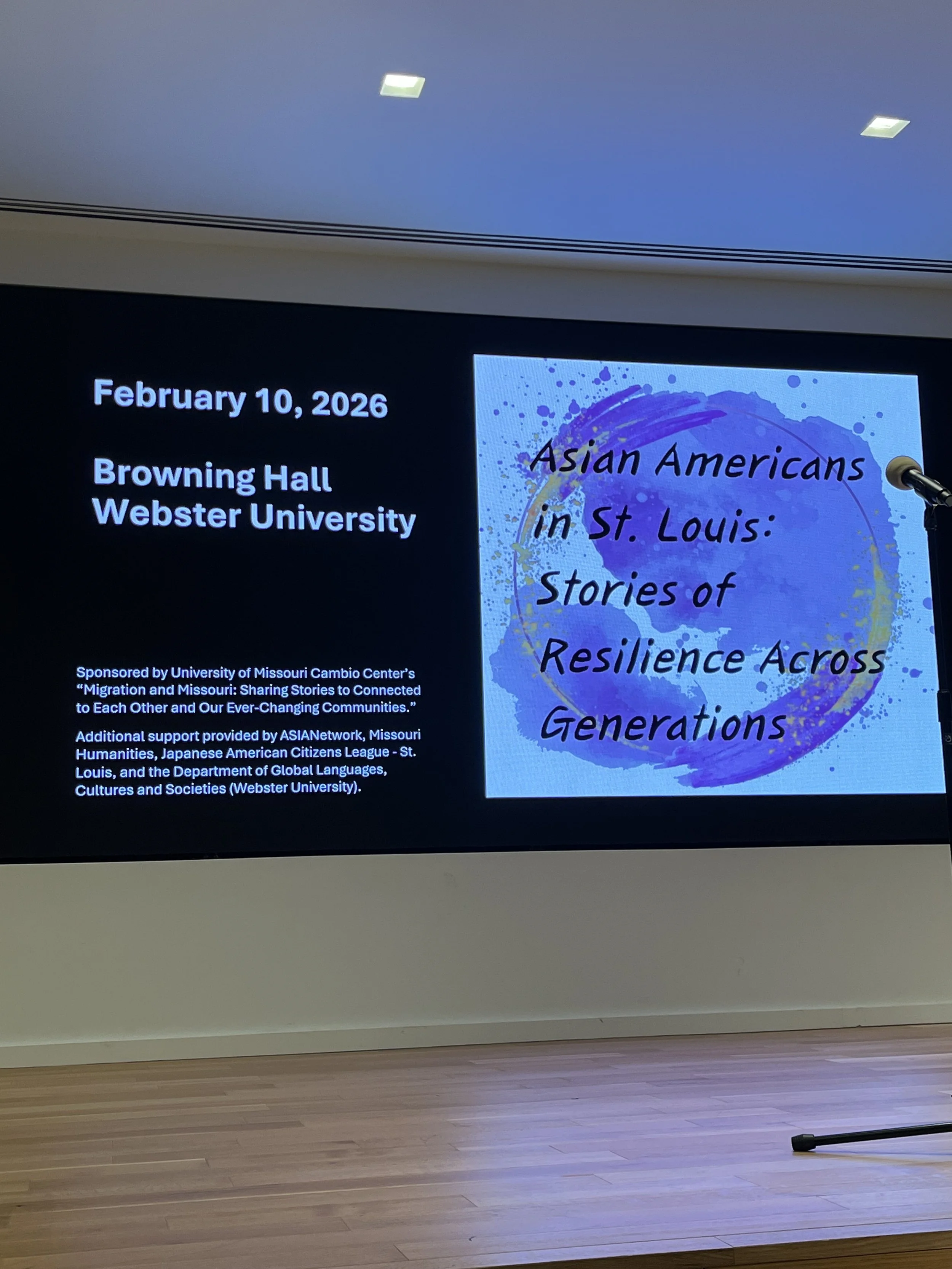 Presentation slide displaying event details: February 10, 2026, Browning Hall, Webster University. Title of presentation: 'Asian Americans in St. Louis: Stories of Resilience Across Generations.' Sponsored by University of Missouri Cambio Center, Asianetwork, Missouri Humanities, Japanese American Citizens League - St. Louis, and Department of Global Languages, Cultures and Societies. A microphone is positioned on the right side of the slide.