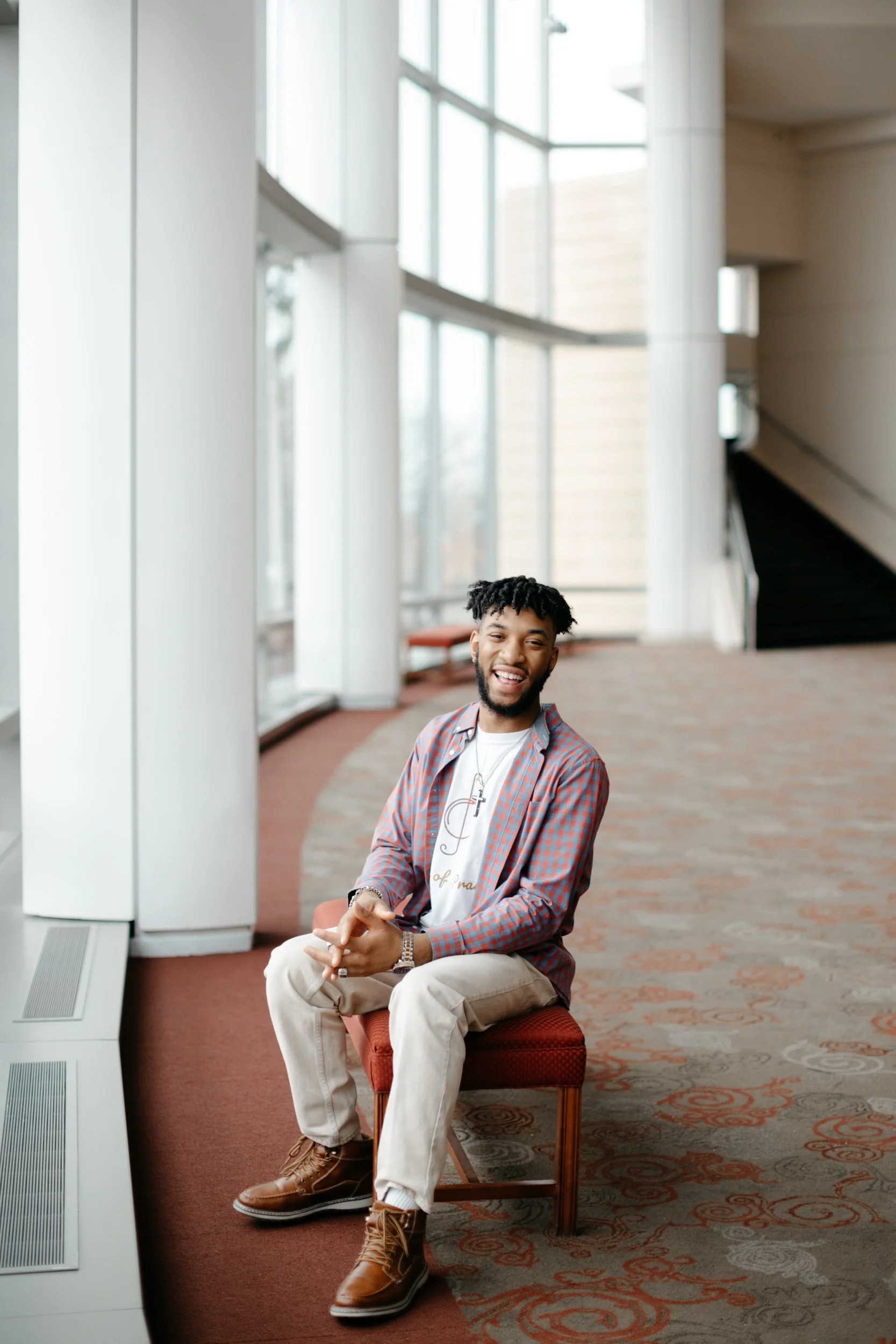 An African American student sits on a bench next to a wall of windows, laughing.  Photographed for a Chicago university marketing campaign.