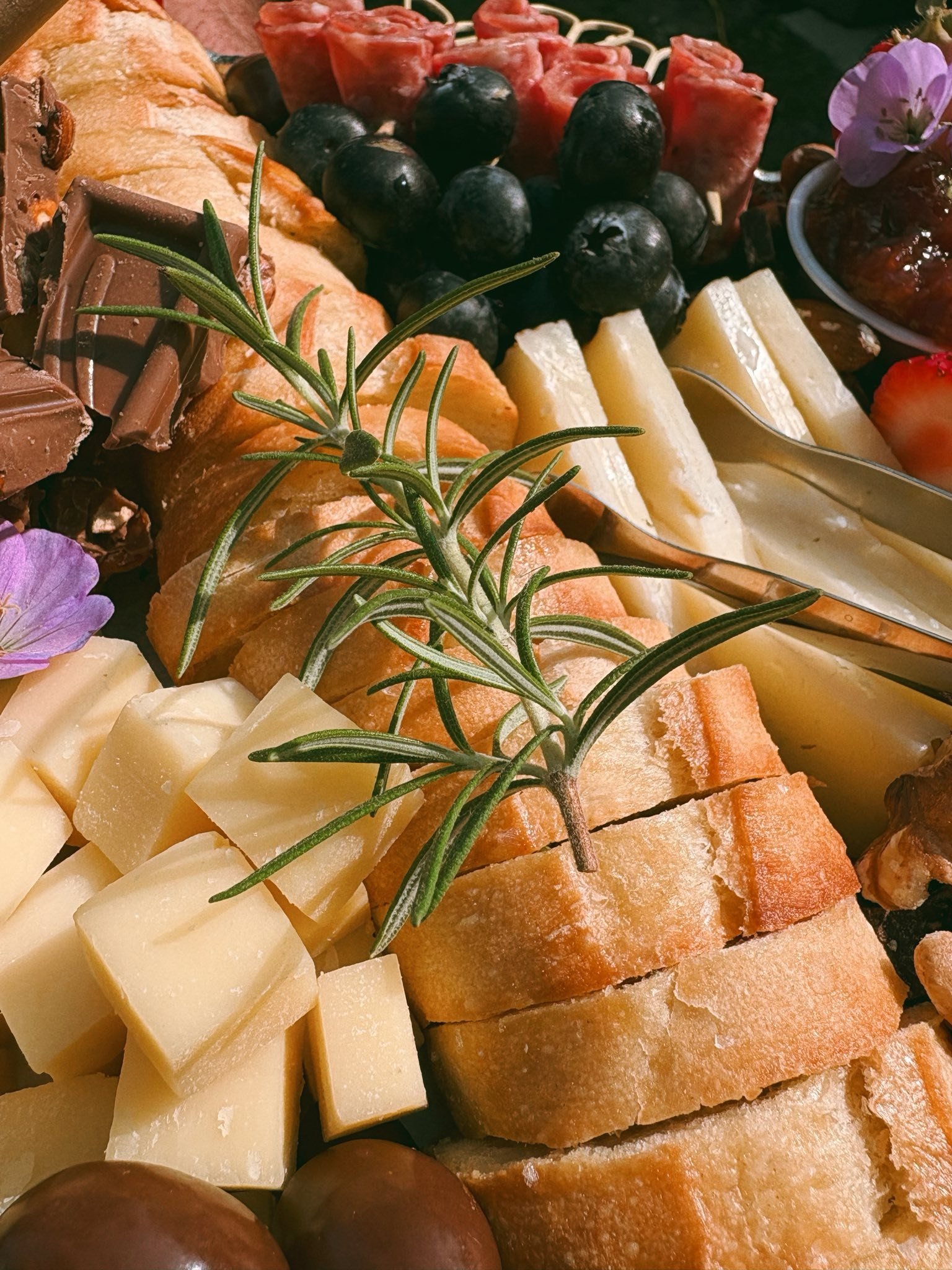 Cheese, grapes, bread, olives, strawberries, and herbs on a platter