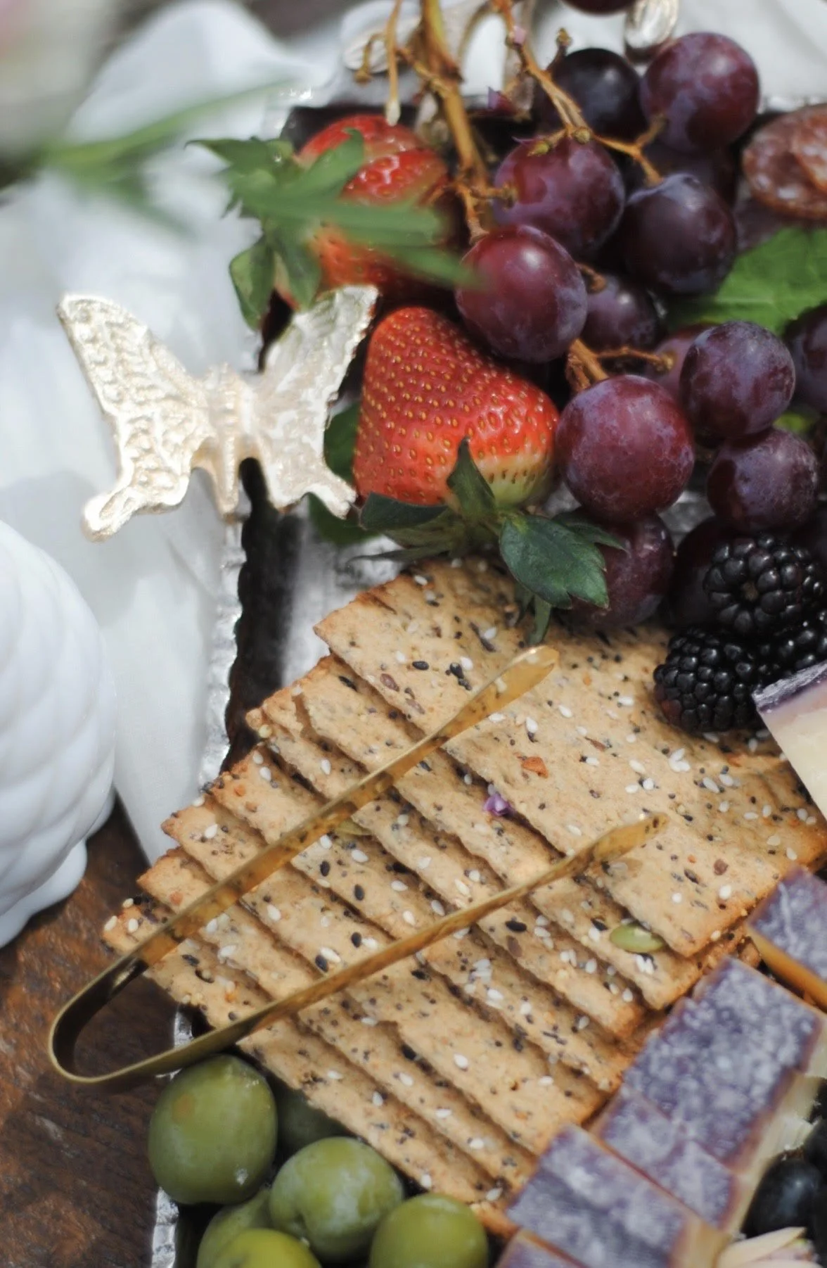 Close-up of a wooden platter with assorted nuts, berries, honeycomb, and a honey dipper, in black and white.