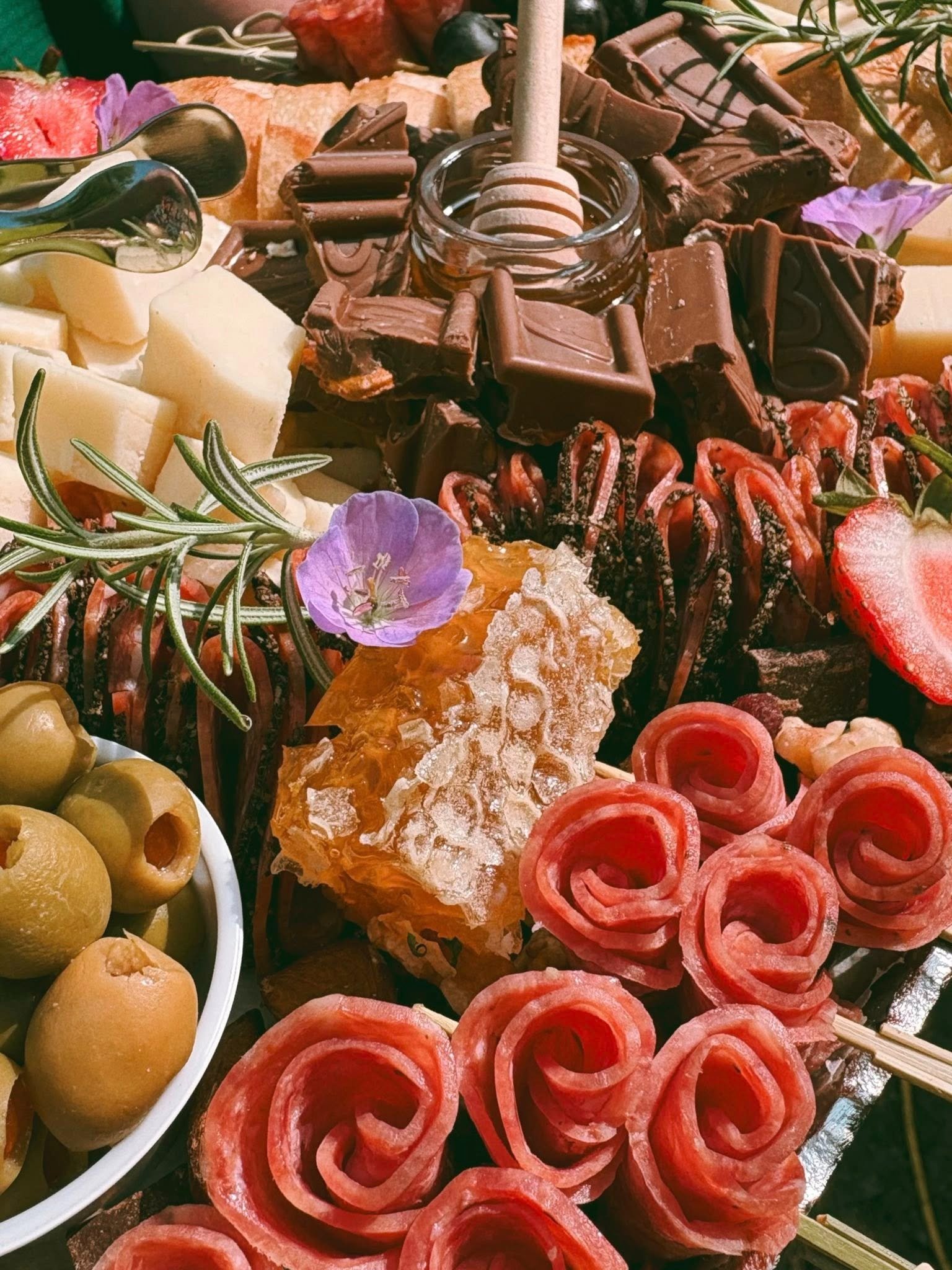 An assortment of chocolates, cheeses, fruits, honeycomb, and garnishes arranged on a platter.