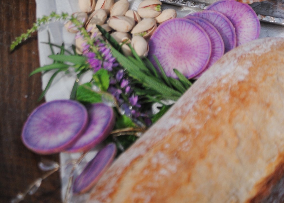 Poisonous mushroom slices, pistachios, pistachio flowers, and a loaf of bread on a wooden surface.