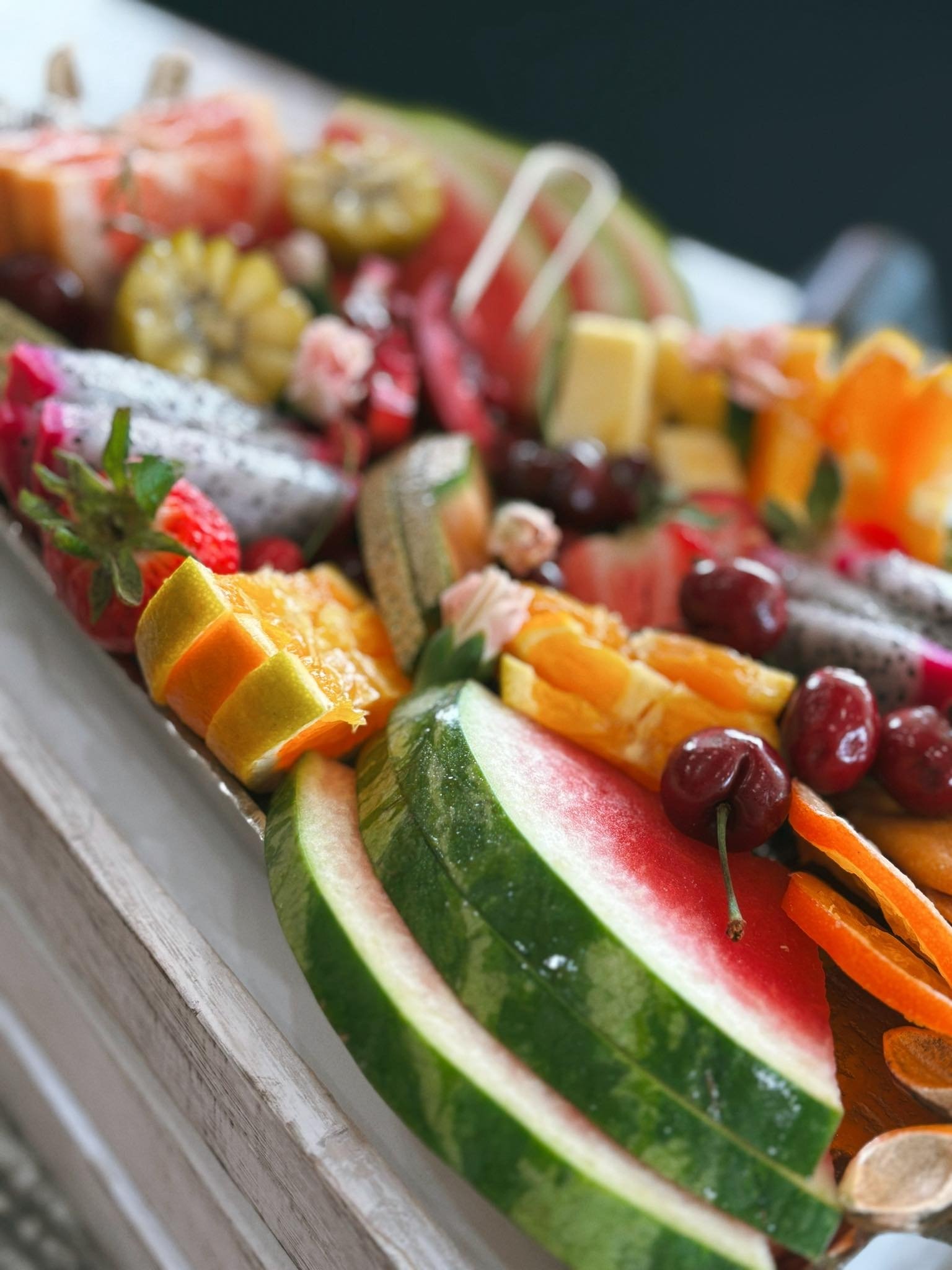 Assorted cut fruit including watermelon, cherries, oranges, strawberries, kiwis, and others arranged on a white platter.