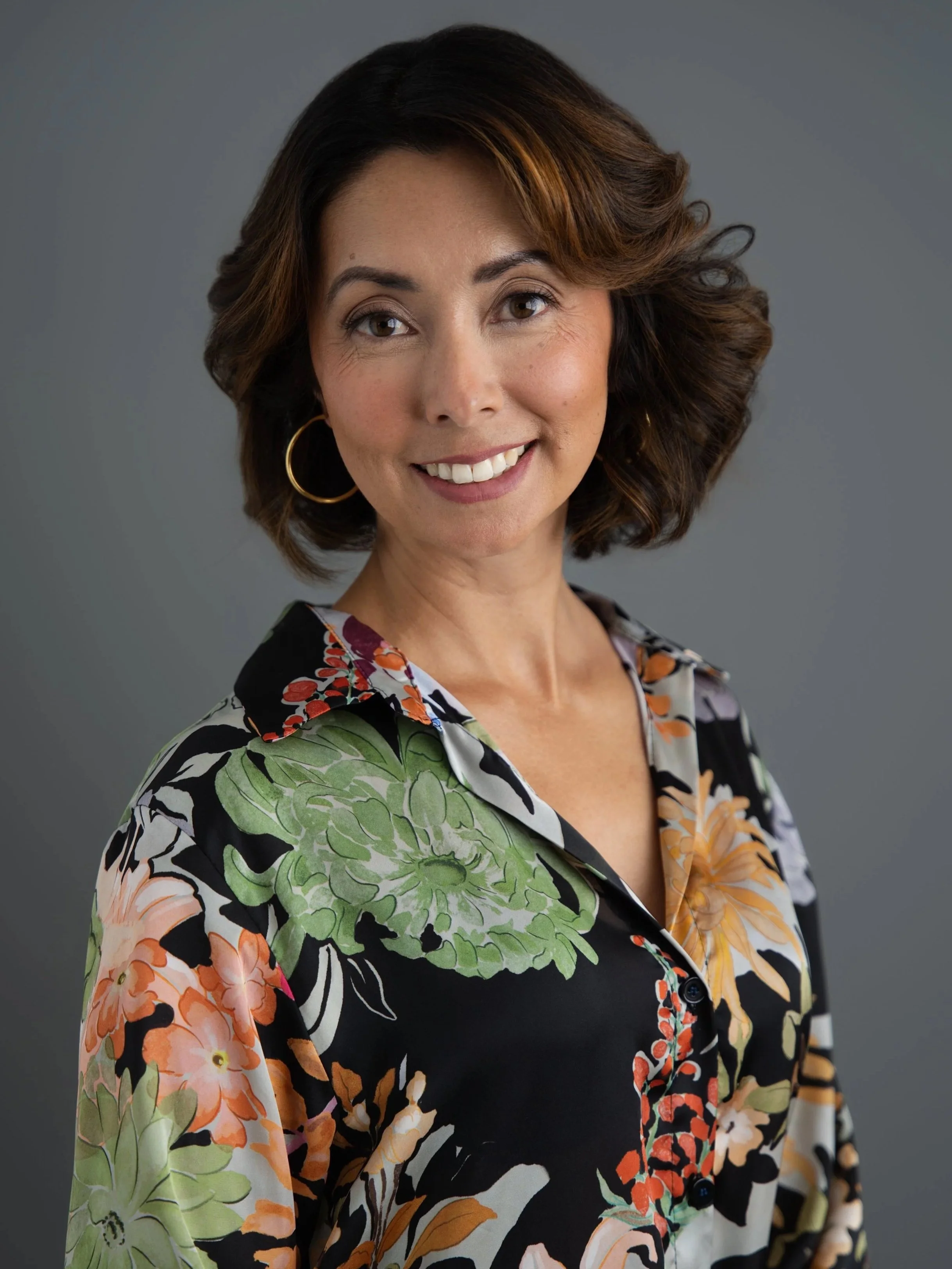 A woman smiling outdoors near a body of water and waterfall.