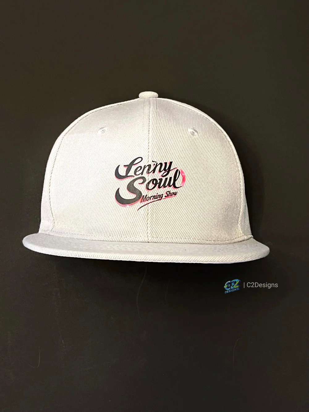 White baseball cap with 'Penny Soul Morning Show' logo on the front, placed on a black surface.