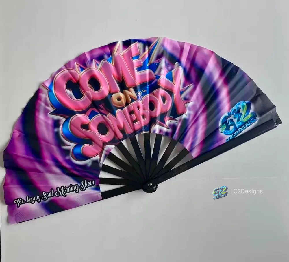 A foldable hand fan with a design featuring the text "Come on Somebody" in large, colorful letters. The background has purple and pink swirls, and there is a small logo in the bottom right corner that says "C2Designs."