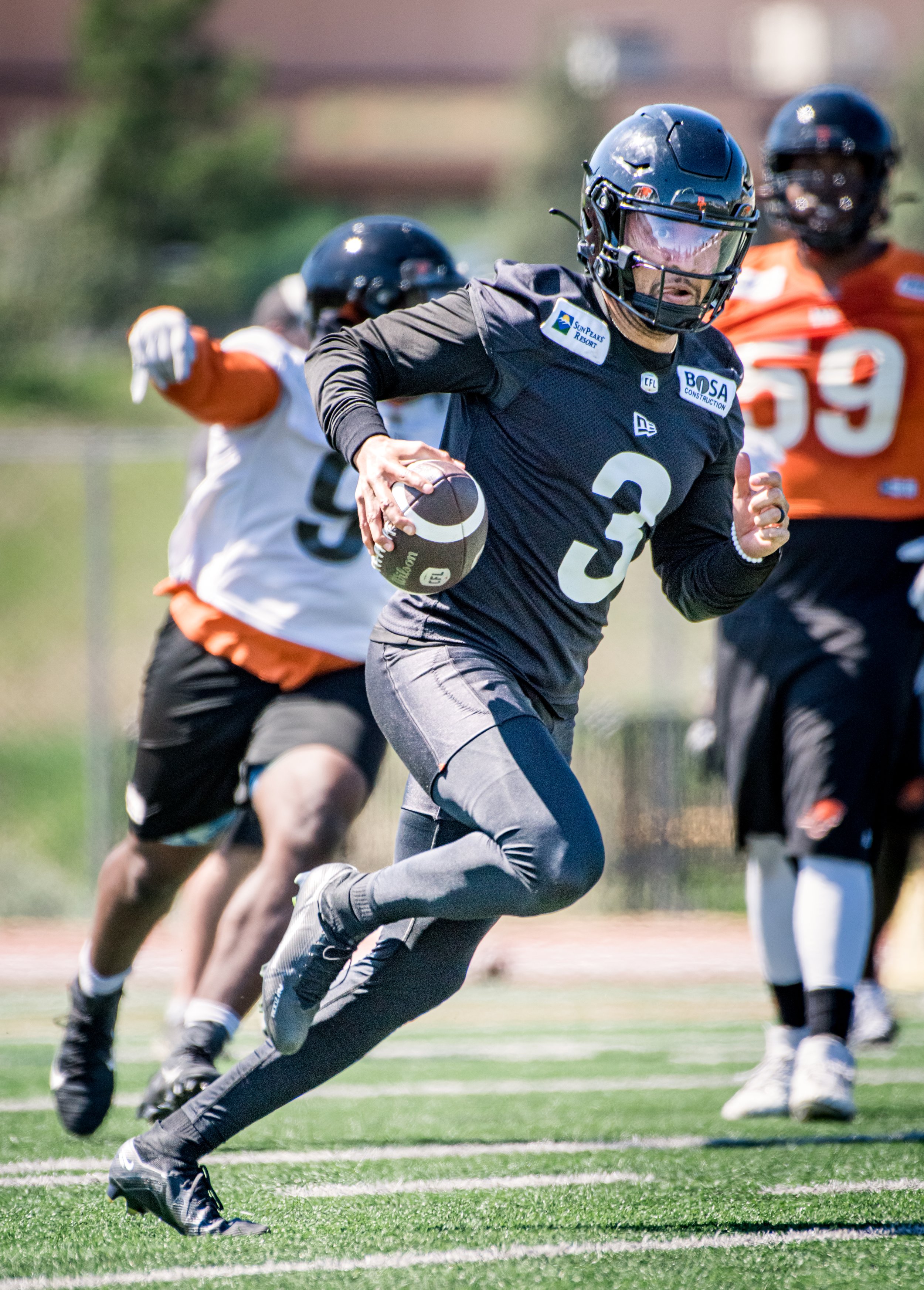 Football player in black uniform running with the ball during practice.