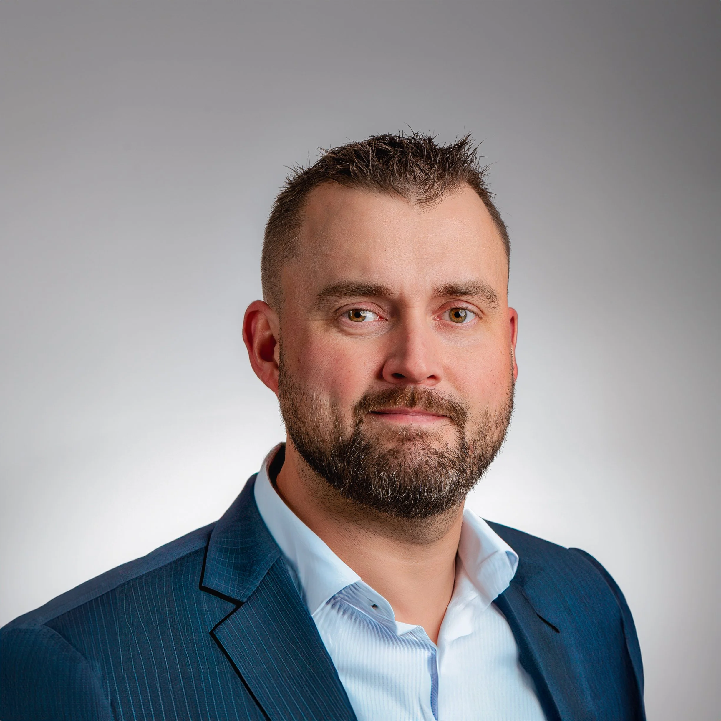 Man in a suit posing for a professional portrait with a light grey background.