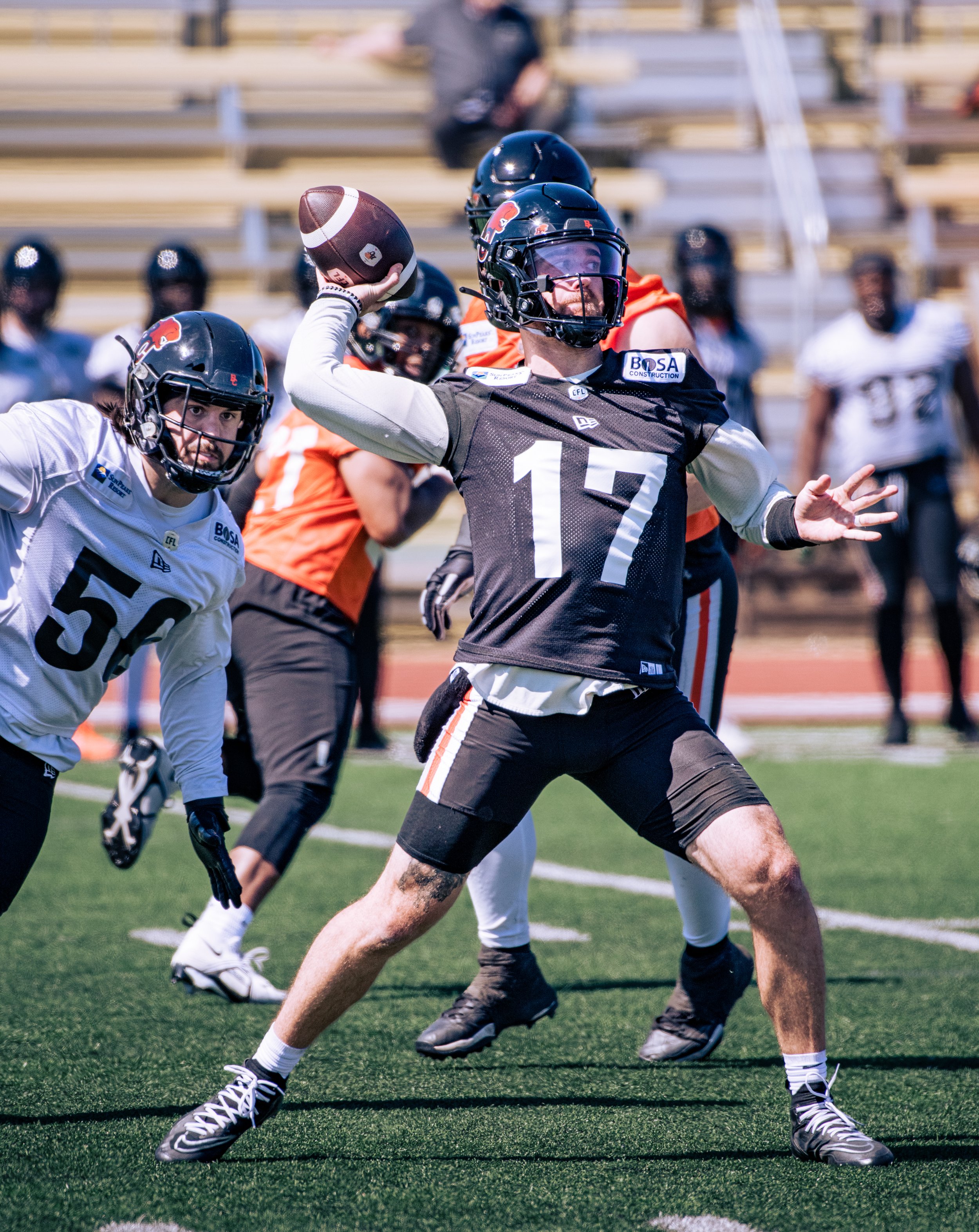Football player in black jersey throwing a ball during practice on the field.