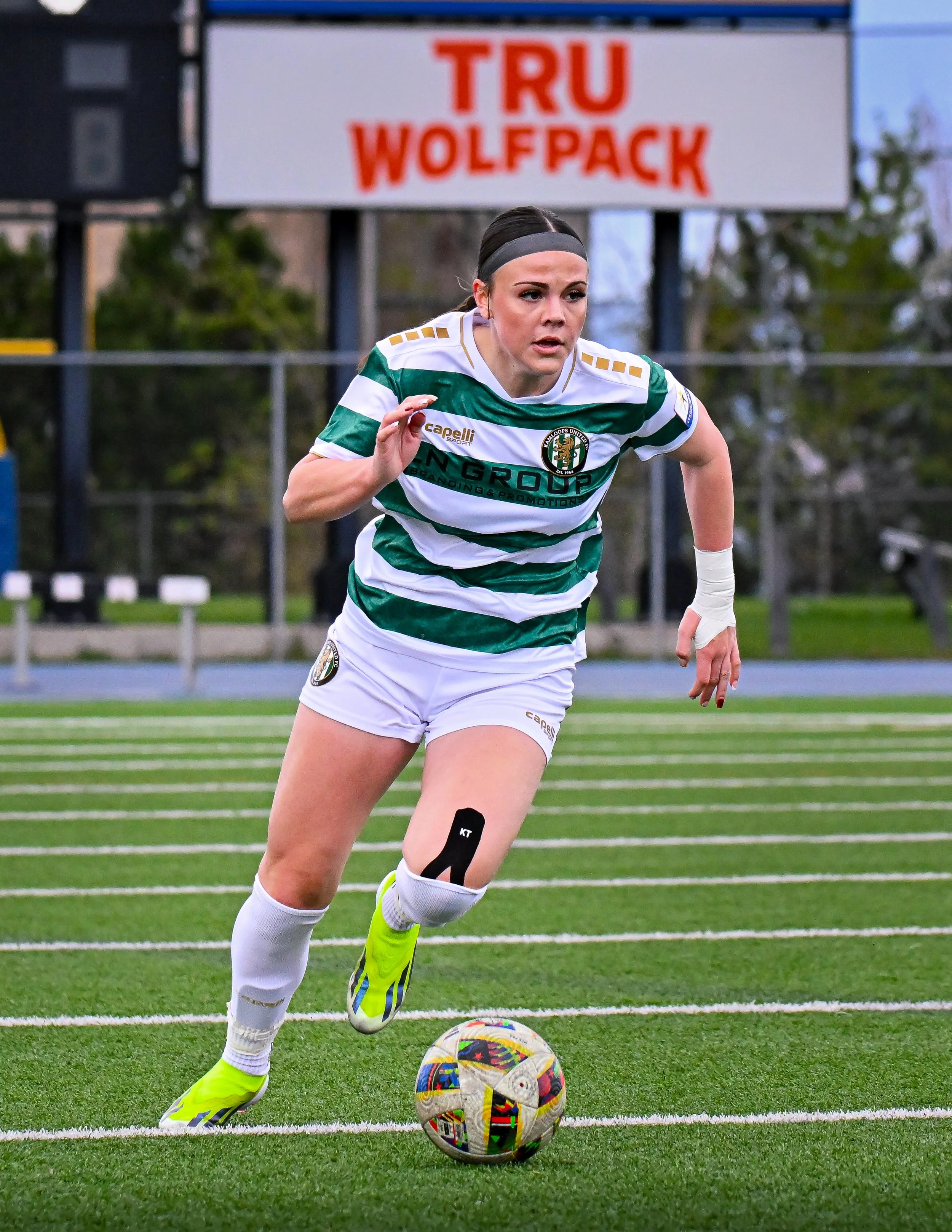 Soccer player in green and white striped jersey running with a ball on a field