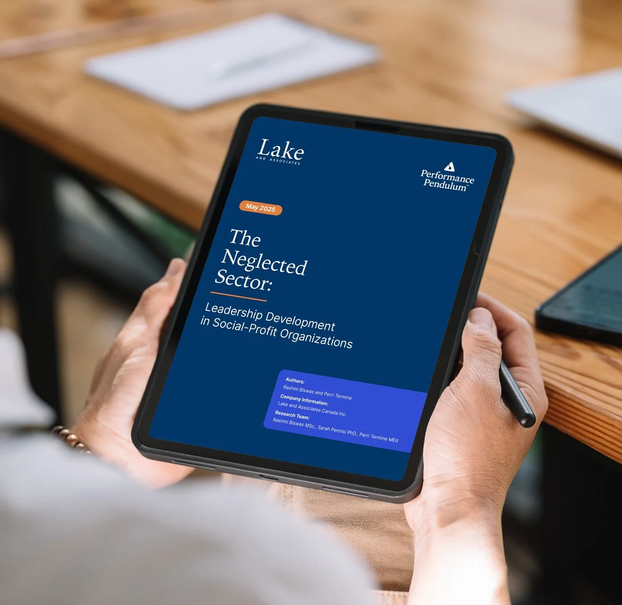 A person holding a tablet displaying a report titled "The Neglected Sector: Leadership Development in Social-Profit Organizations" from Lake and Associates, with a blue background and white text.
