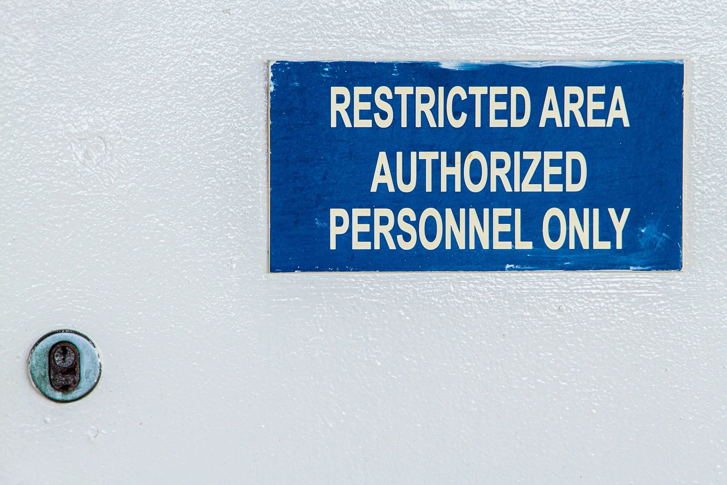Blue sign on a white wall reads, 'Restricted Area Authorized Personnel Only'.