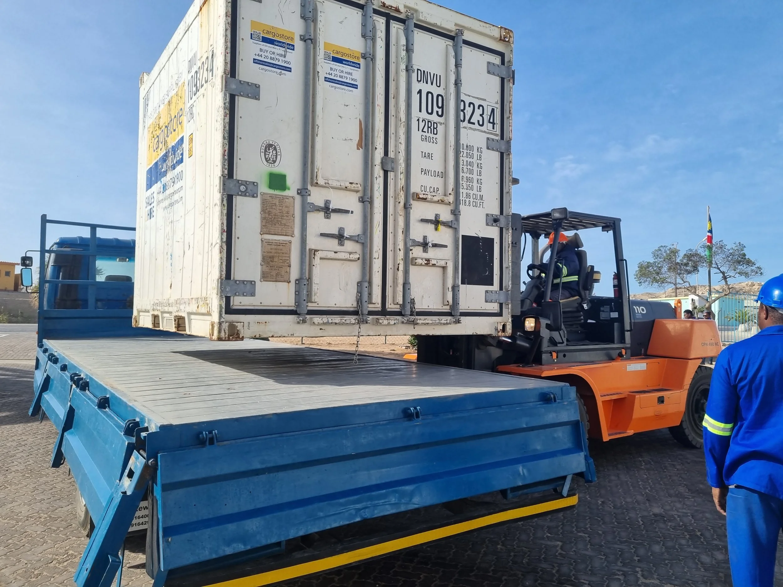 A person in a red shirt is loading Coca-Cola crates onto a red delivery truck on a city street.