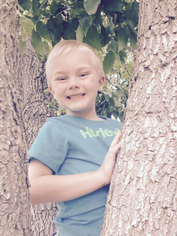 child smiling while leaning up to a tree