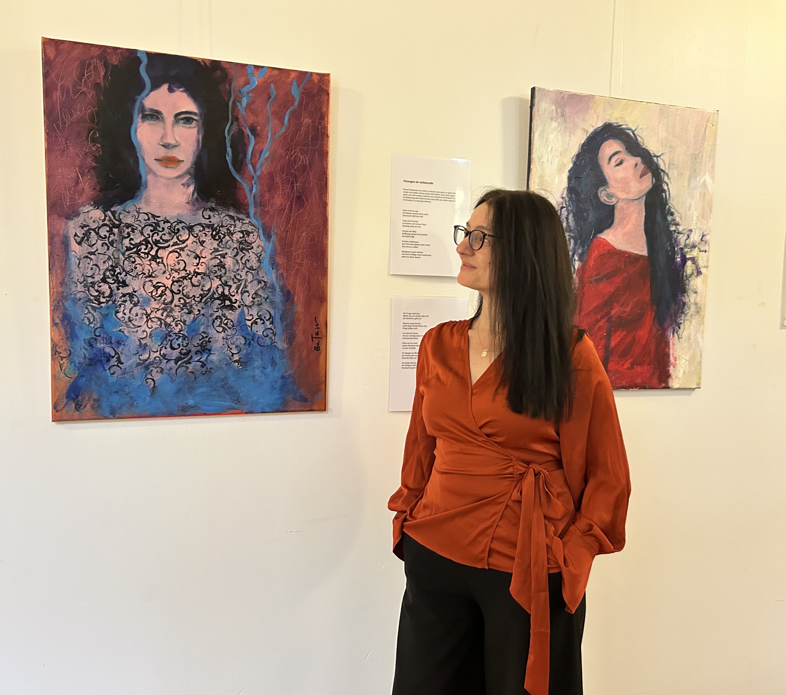 Frau mit dunklem Haar und Brille betrachtet Gemälde von zwei Portraits einer Frau in einer Kunstgalerie.