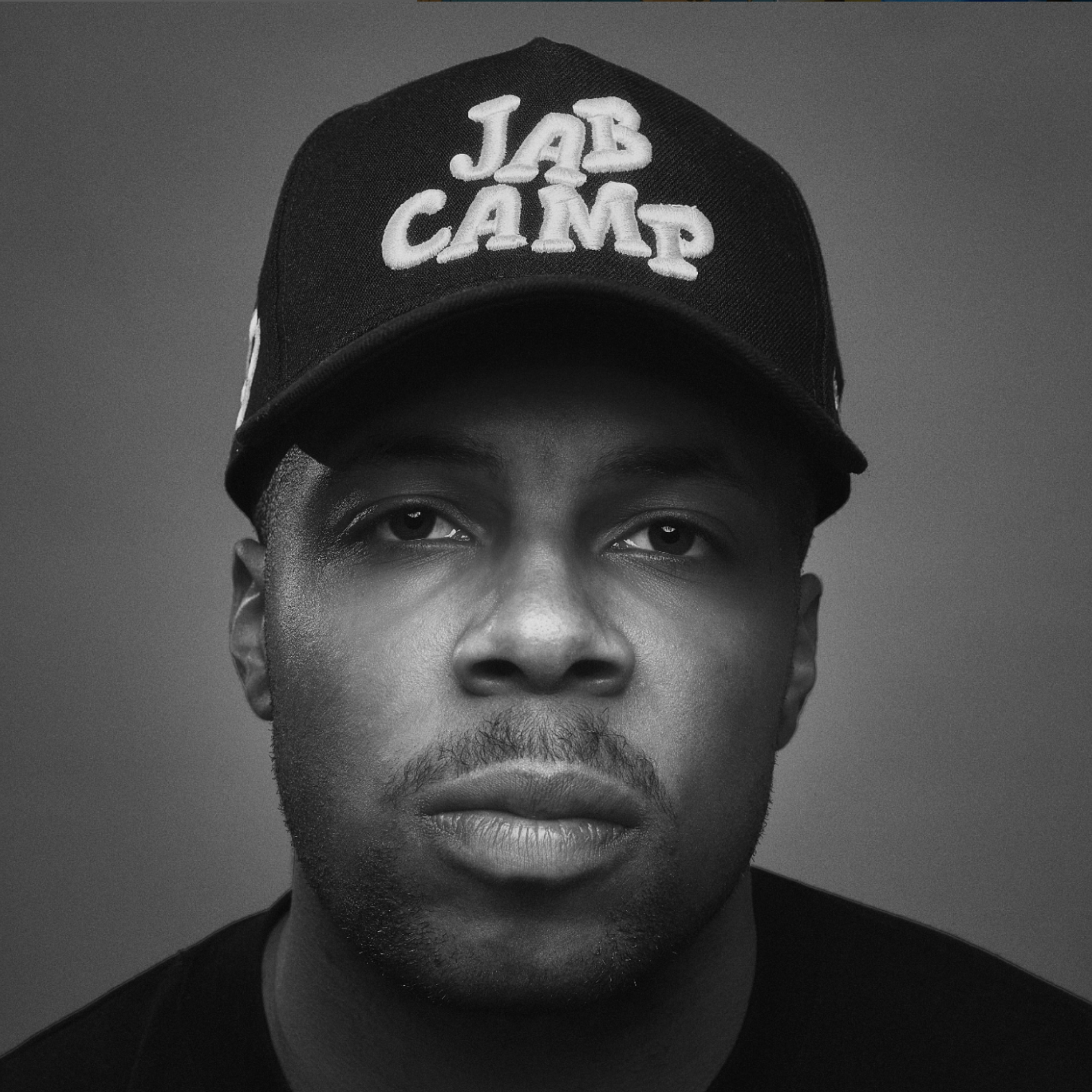 Black and white close up portrait of Jared Armstrong wearing a JAB Camp baseball cap looking directly at the camera