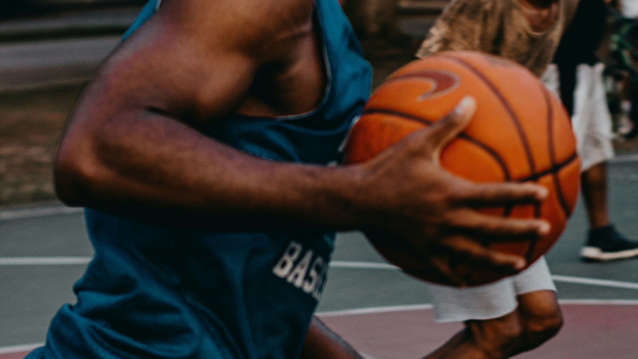 Close up action shot of a basketball player gripping a basketball on an outdoor court with shallow depth of field and blurred background players