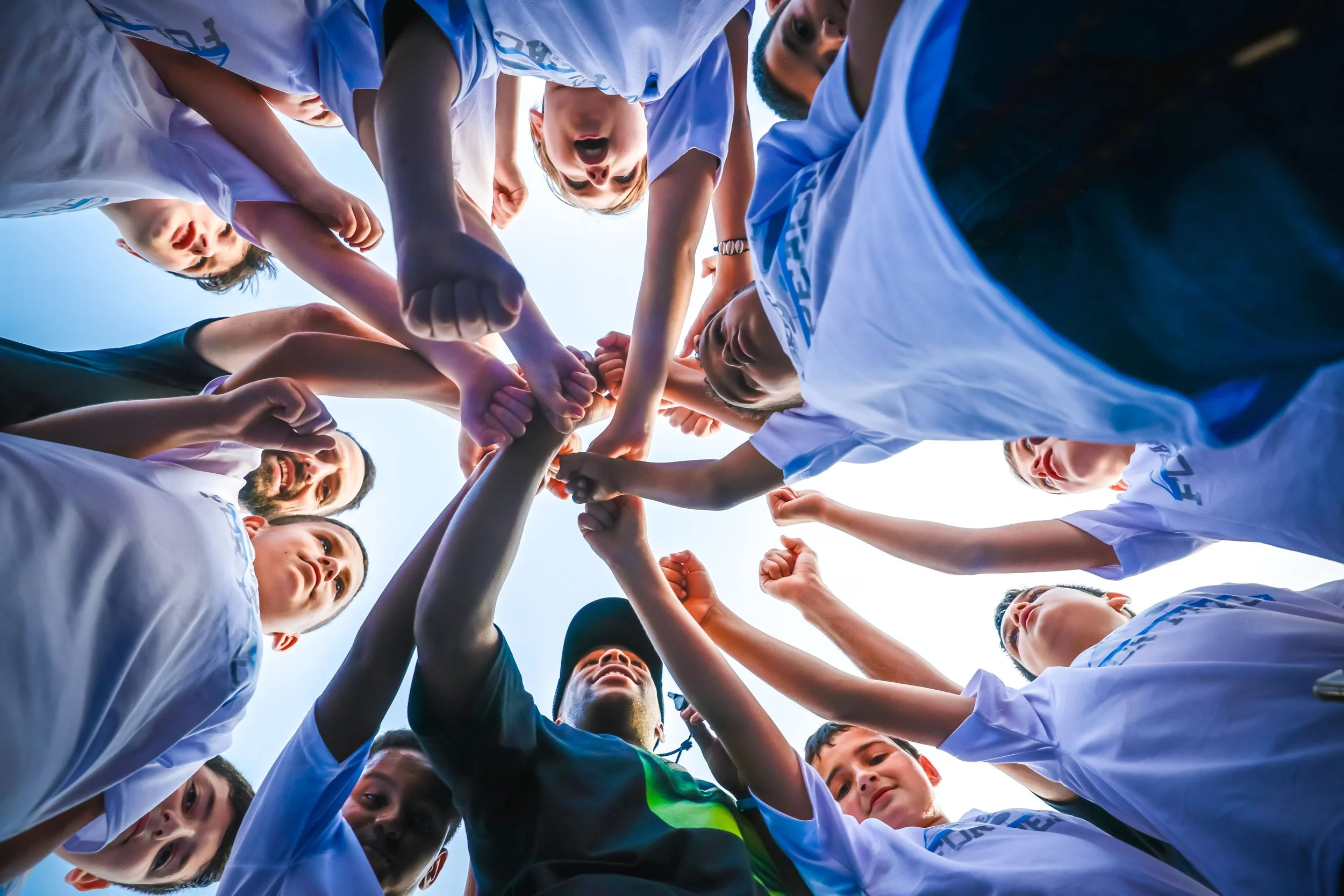 Group of young basketball players standing in a circle with hands stacked together looking up toward the camera