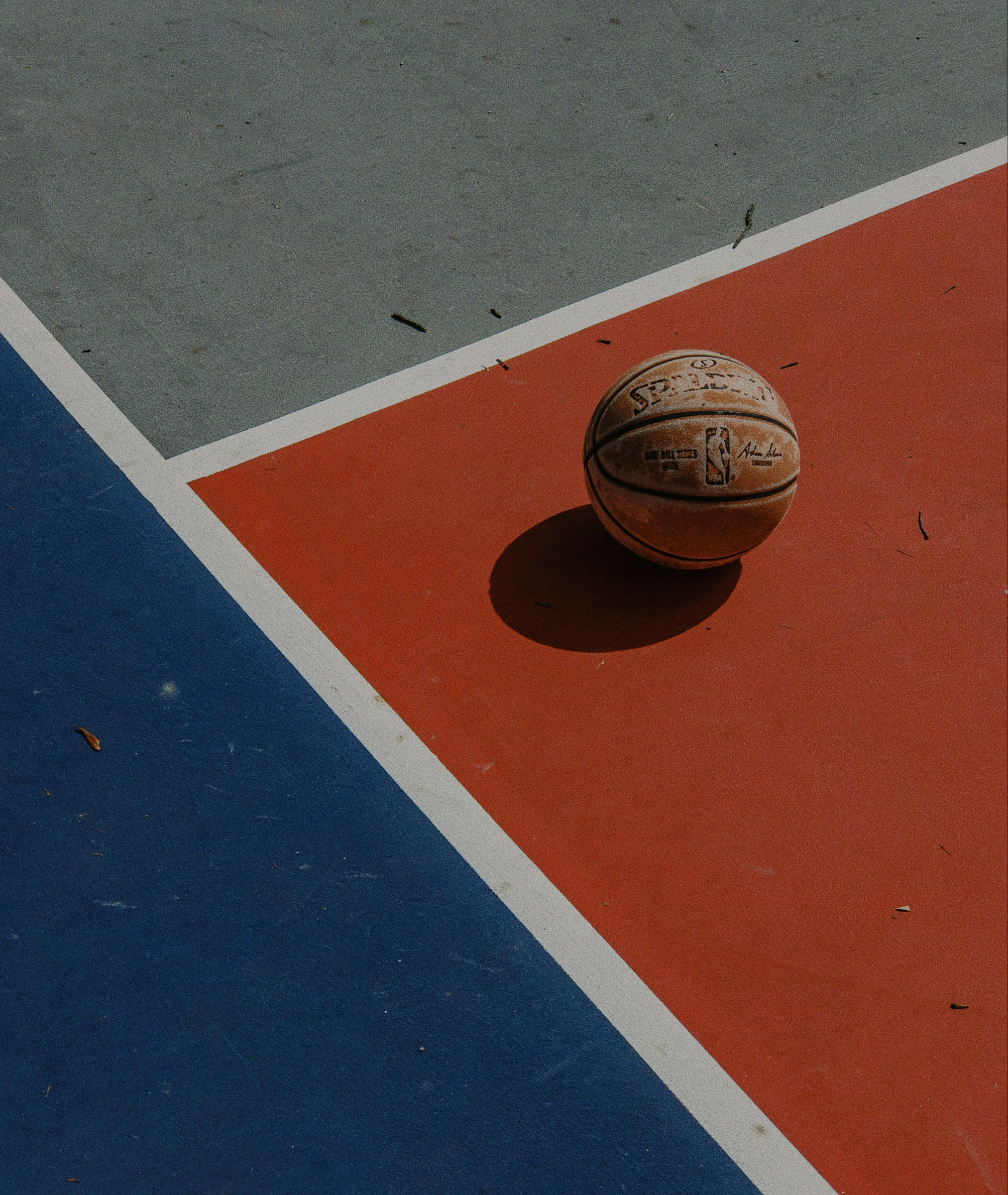 Basketball resting on an outdoor court with red and blue painted surface in bright daylight
