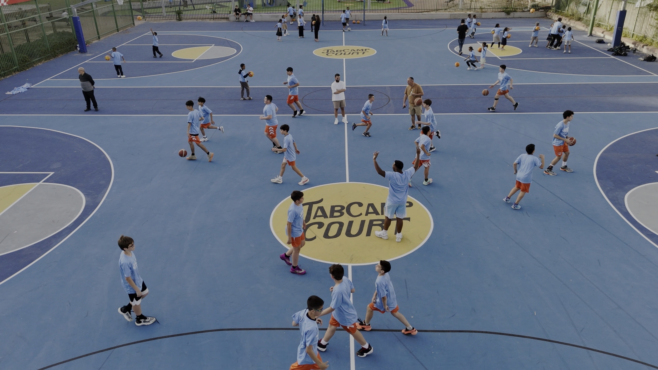 JAB camp participants playing on an outdoor court with a large JAB Camp Court logo at center