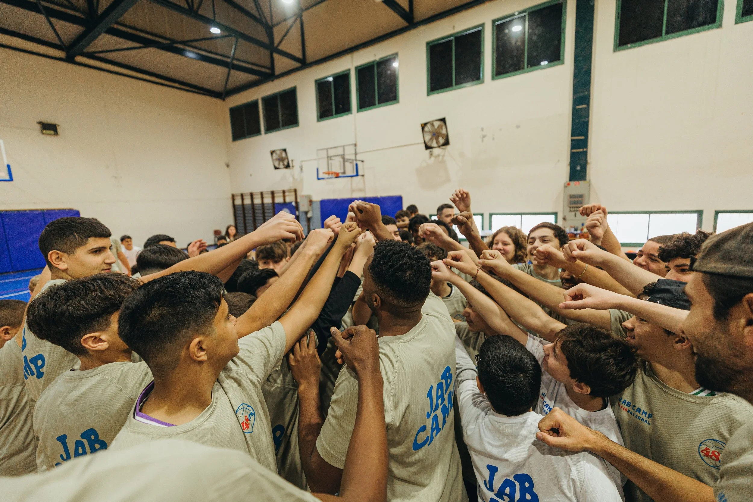 Basketball players in a gym huddled together with arms raised in unity before or after a game
