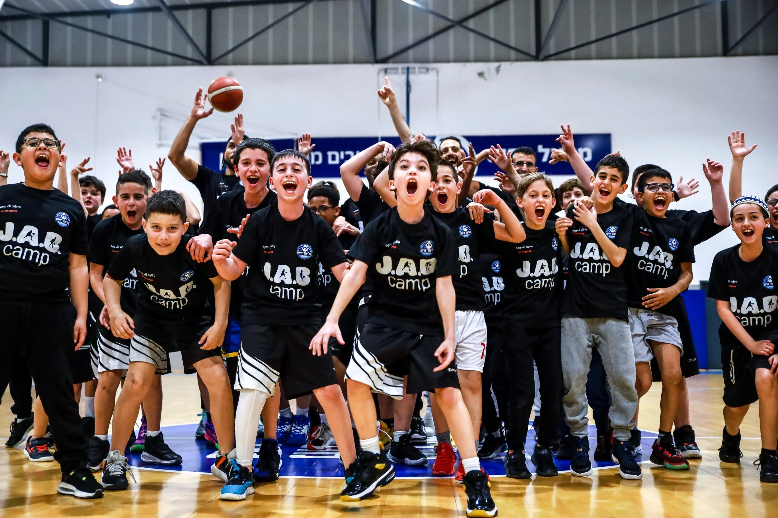 Excited group of youth basketball players in JAB Camp shirts celebrating on an indoor court