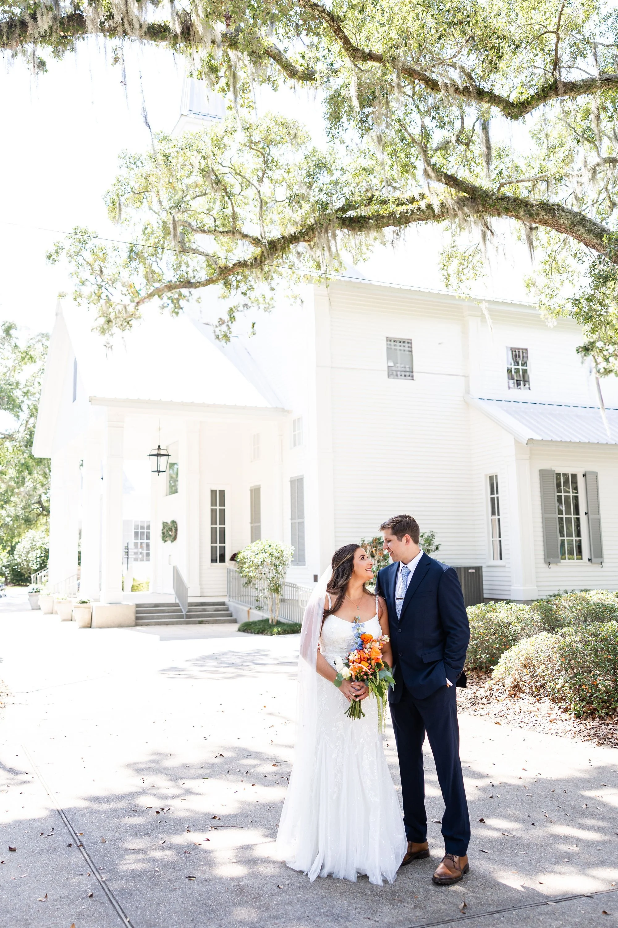 bride-and-groom-smiling-under-a-large-tree-outside-a-white-c.jpg