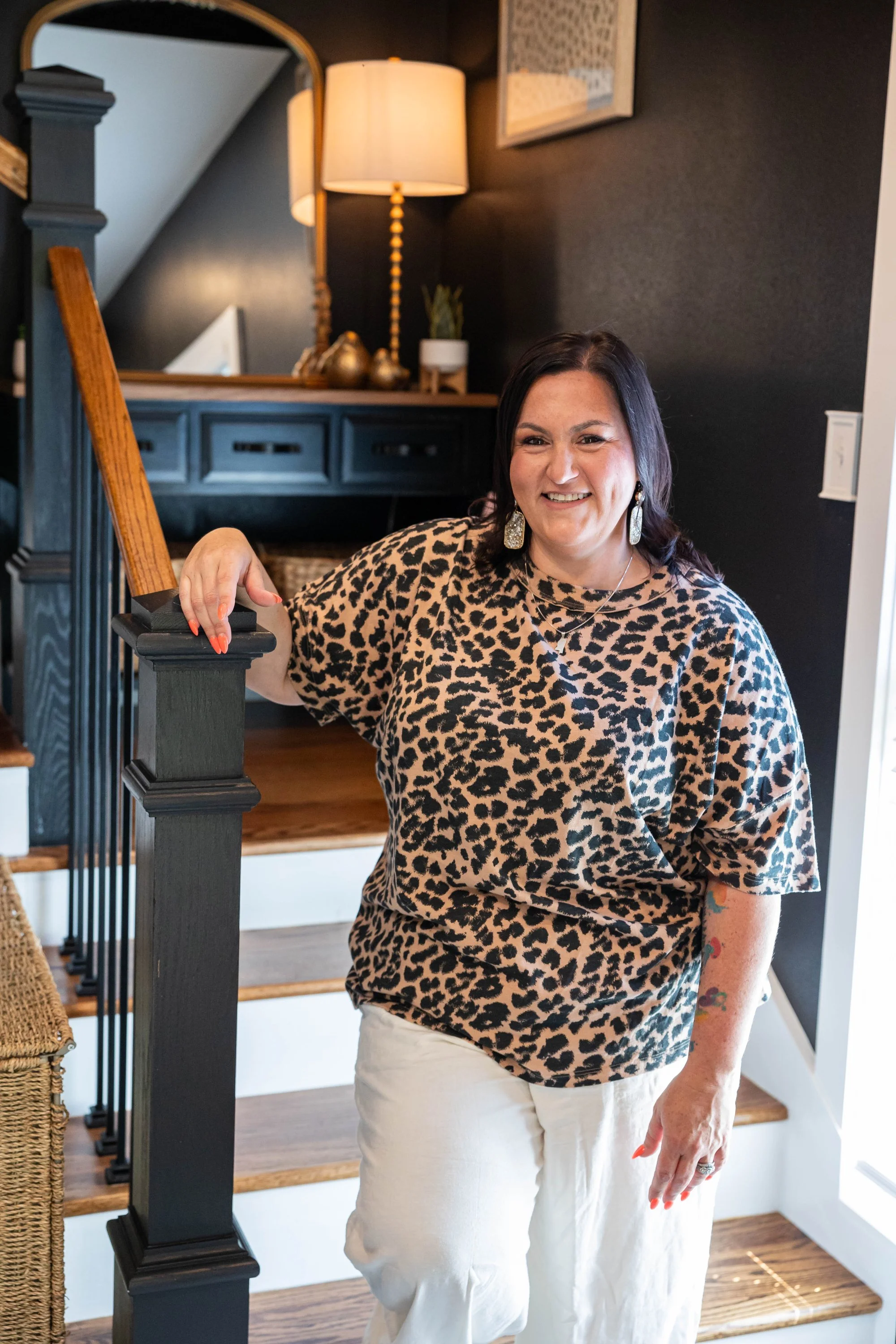smiling-woman-in-leopard-print-top-stands-on-wooden-staircas.jpg