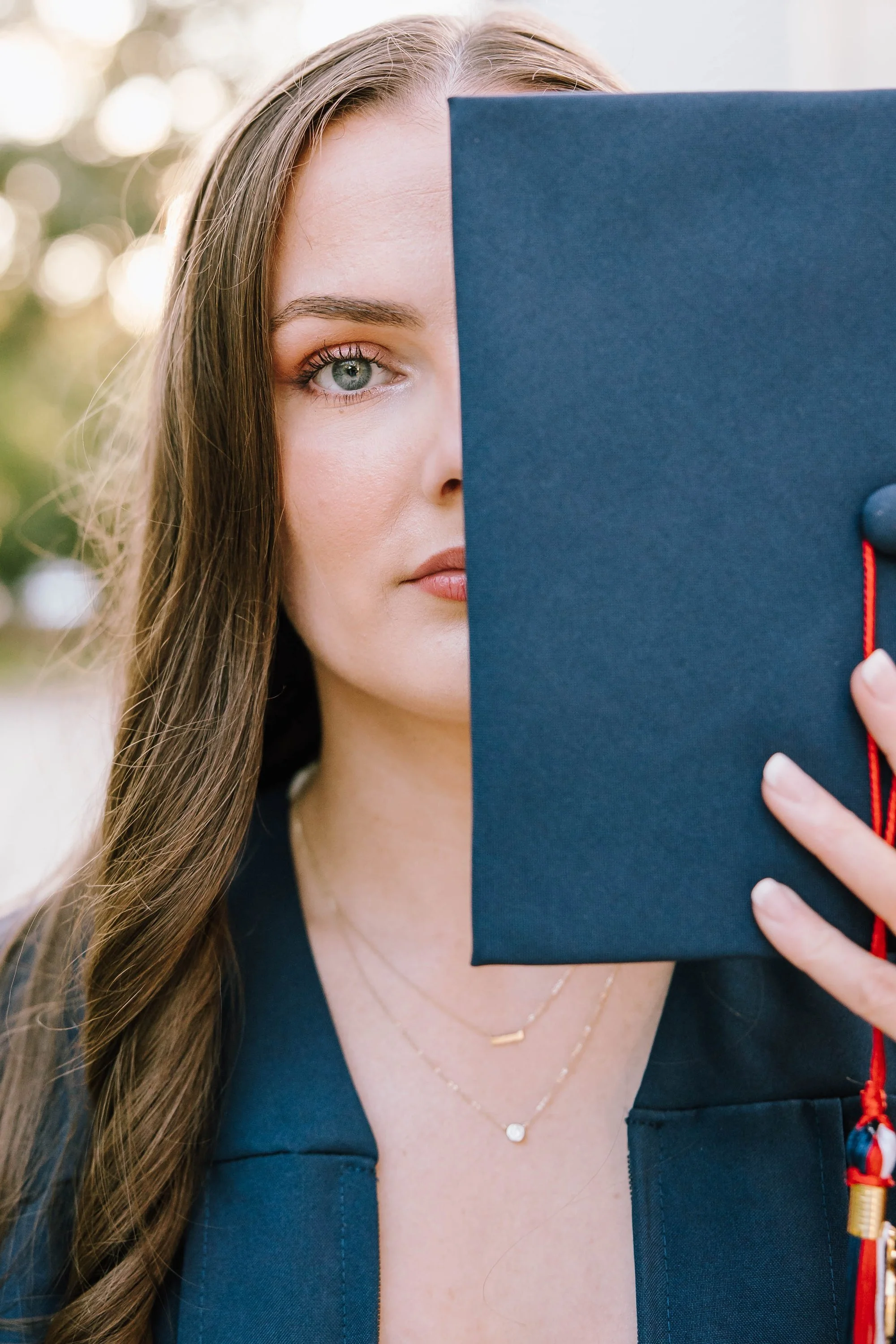 graduate-holding-cap-half-face-visible-with-blurred-outdoor.jpg