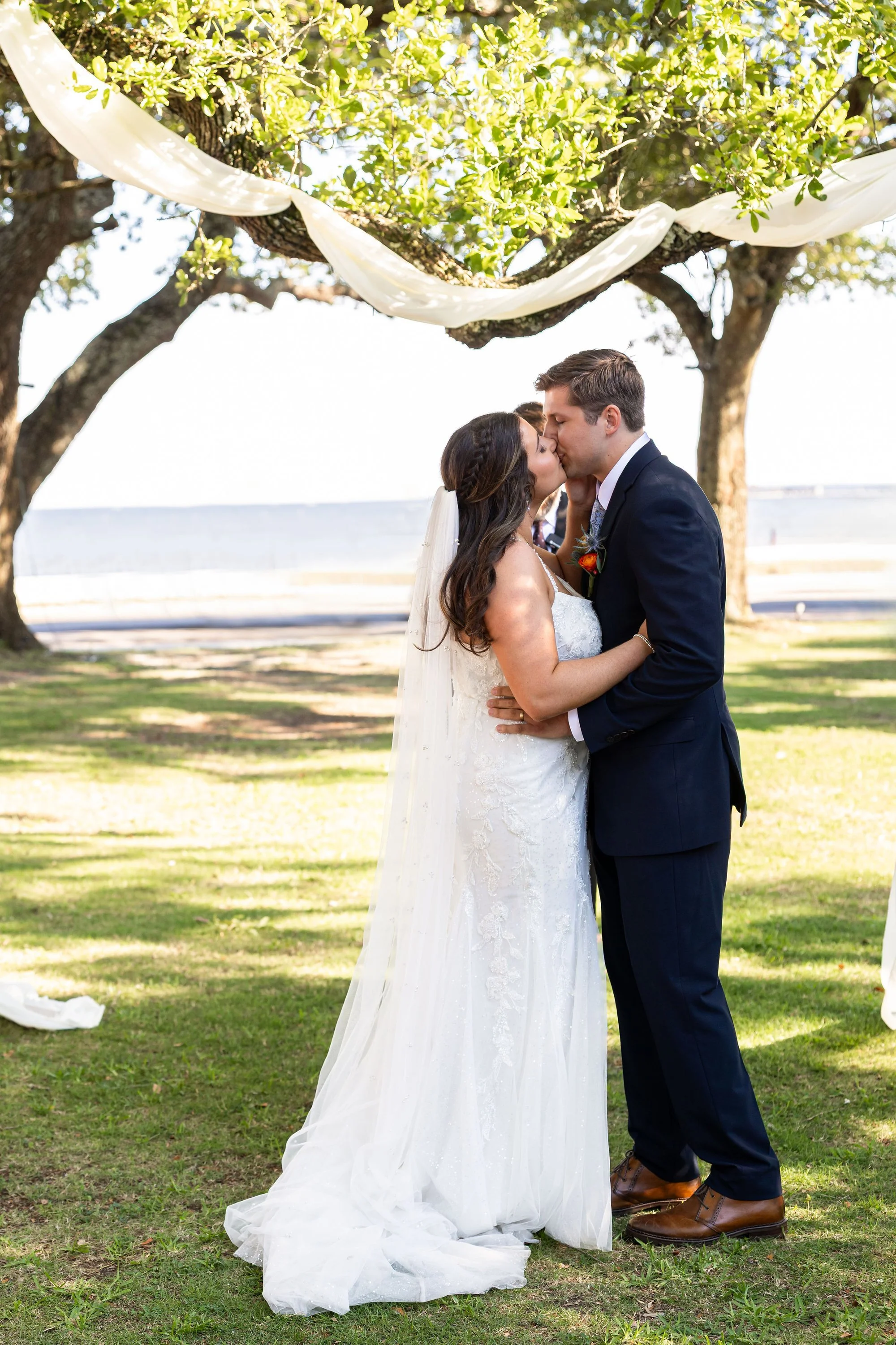 bride-and-groom-kissing-under-draped-tree-with-ocean-in-back.jpg