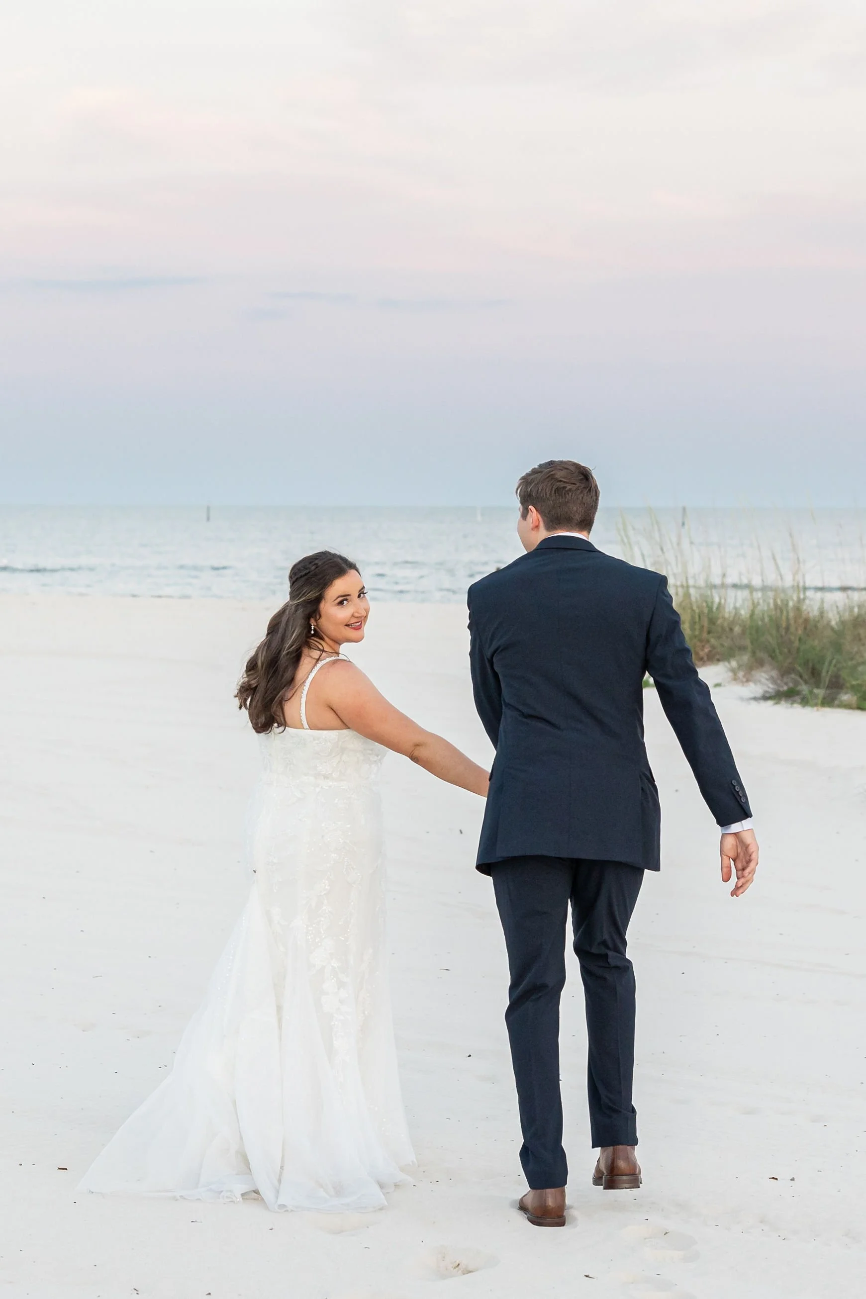 bride-and-groom-walking-hand-in-hand-on-a-serene-beach-at-su.jpg