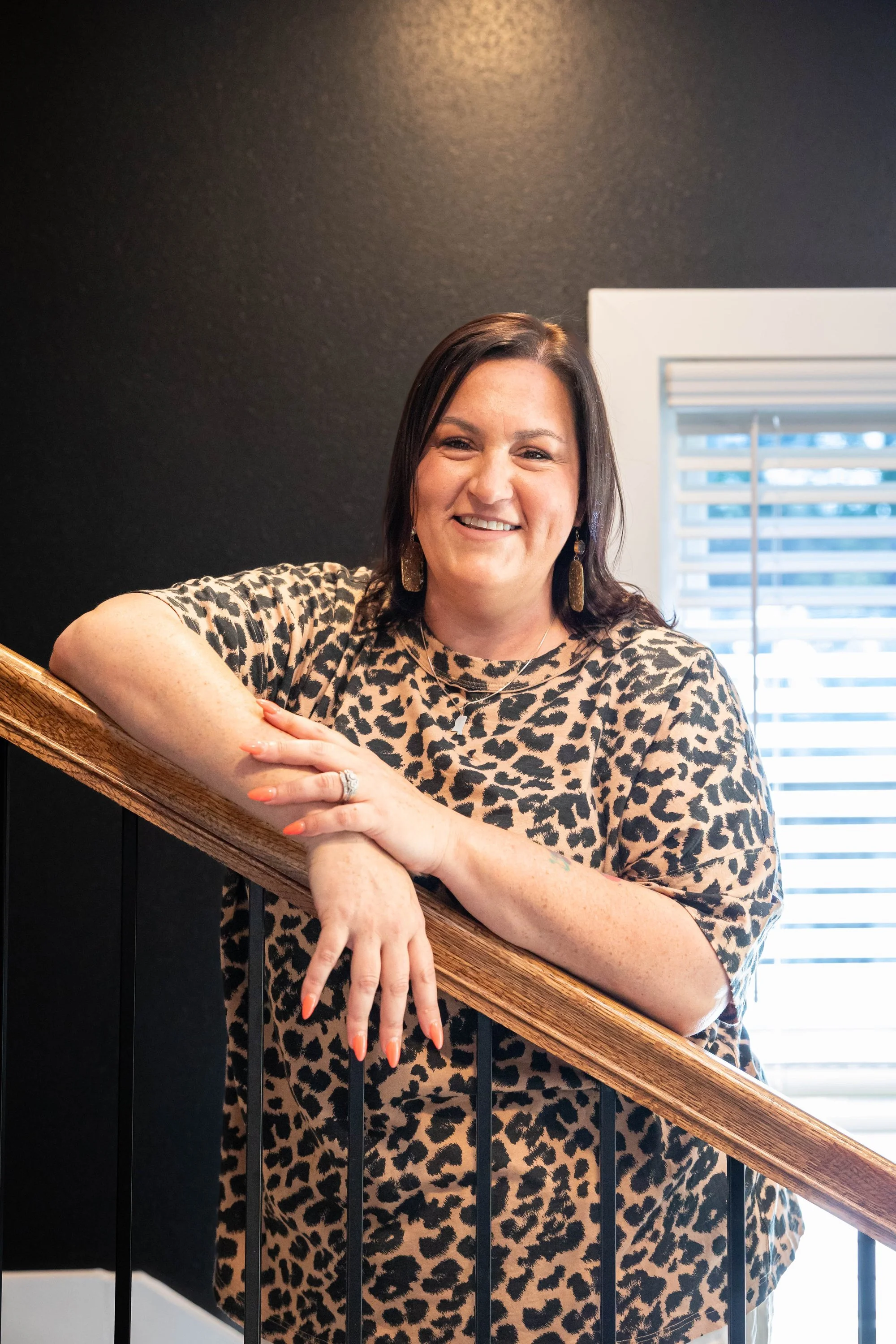 smiling-woman-in-leopard-print-top-leaning-on-a-wooden-stair.jpg