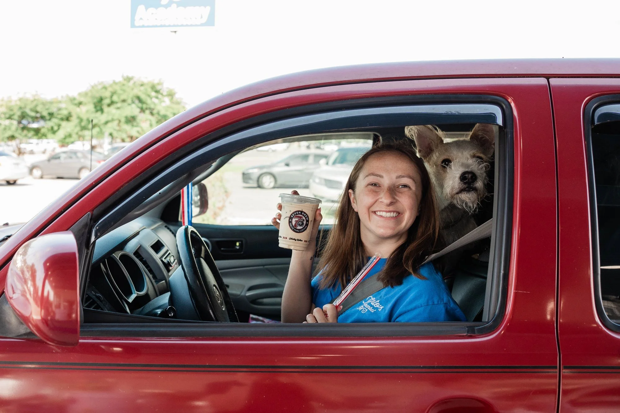 woman-smiling-in-red-car-holding-a-drink-with-a-dog-beside-h.jpg