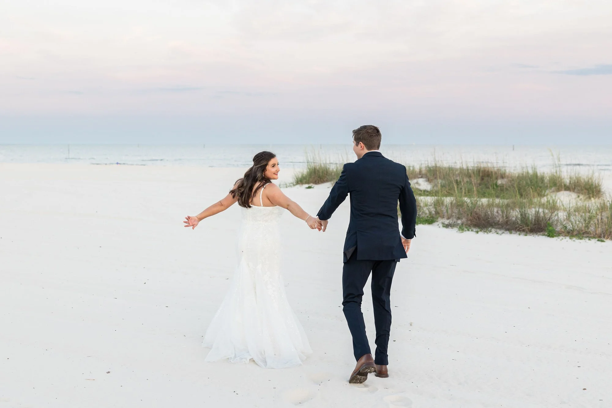 bride-and-groom-holding-hands-walking-on-a-sandy-beach-at-su.jpg