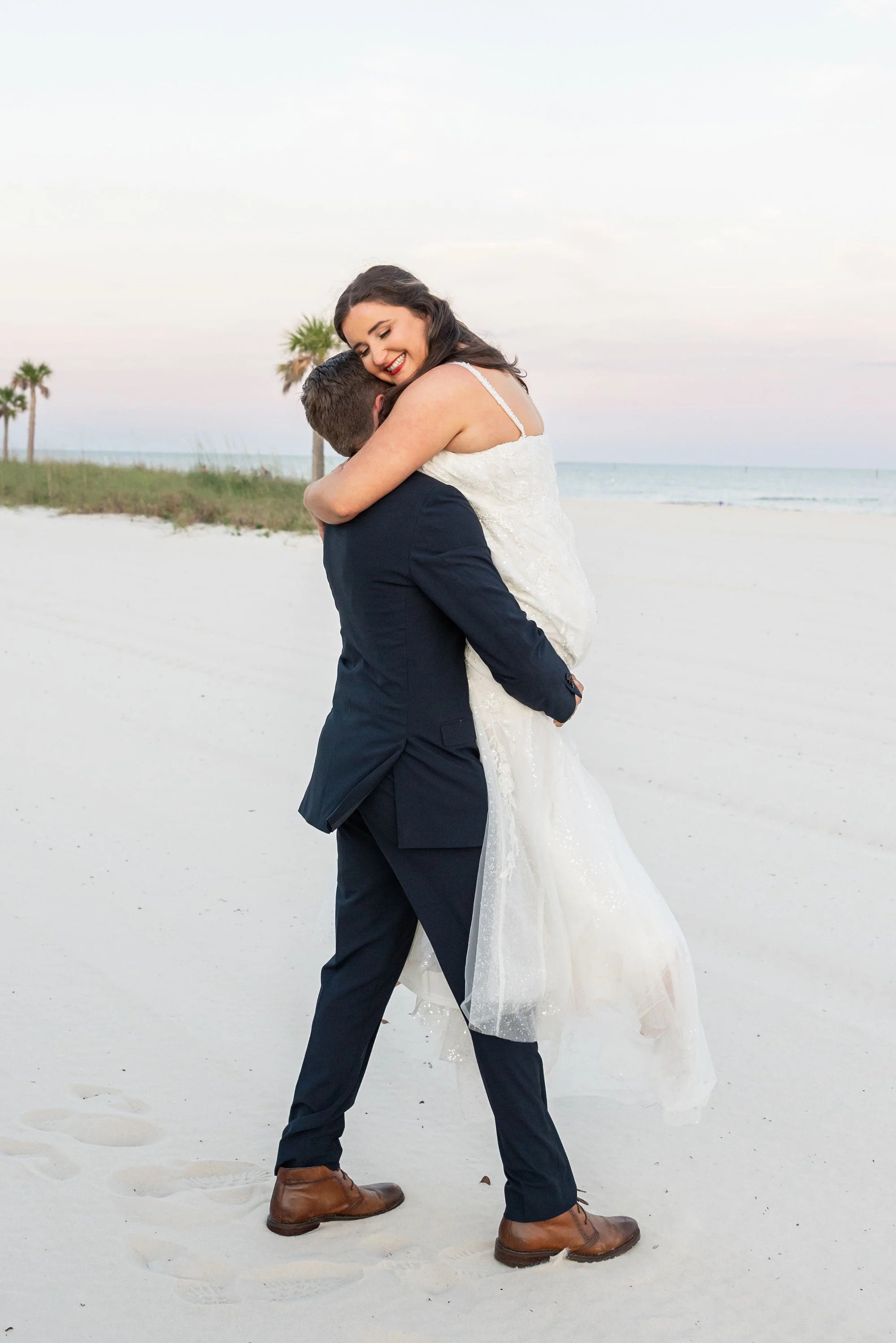bride-in-white-dress-joyfully-lifted-by-groom-on-a-sandy-bea.jpg