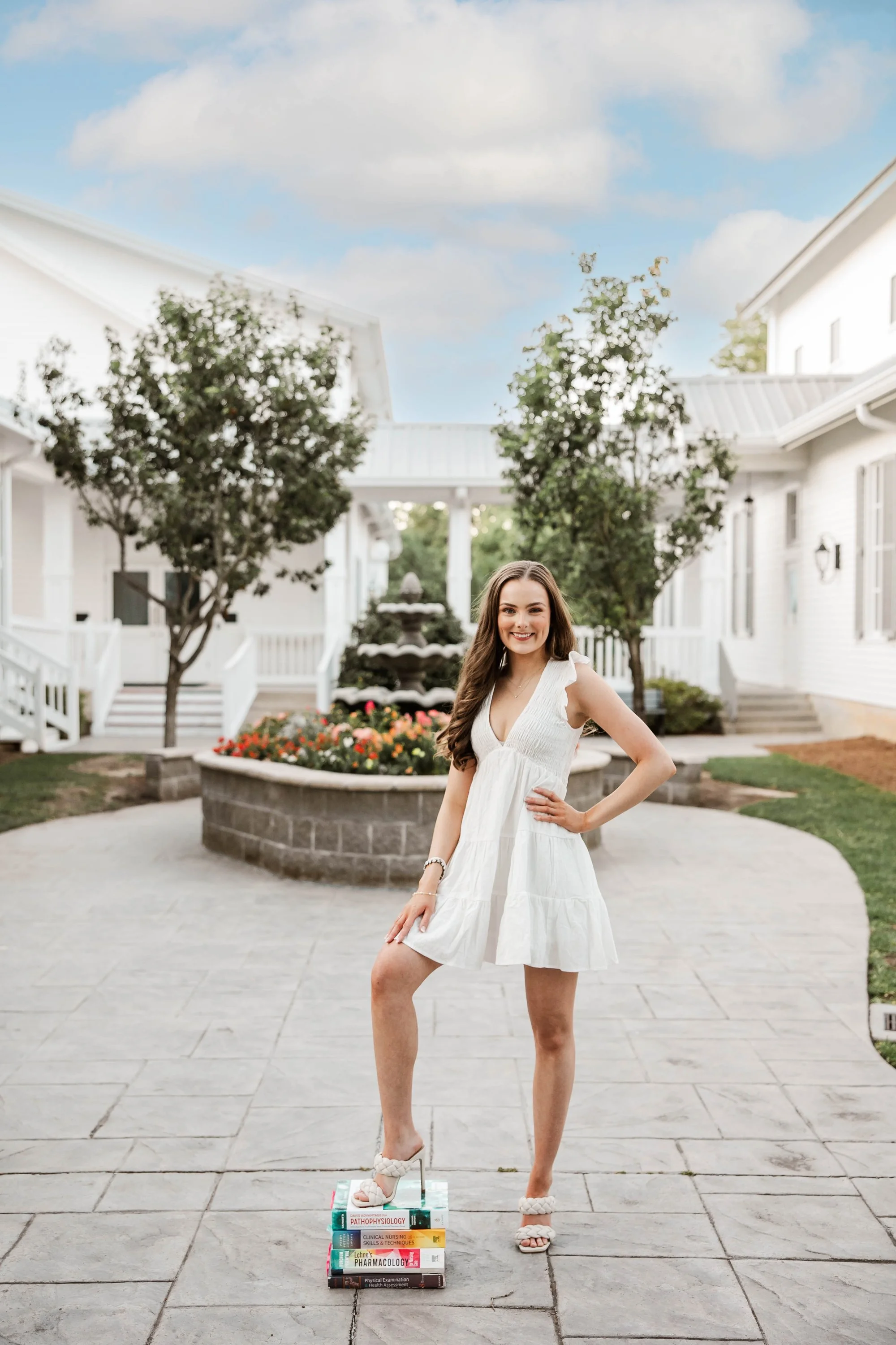 woman-in-white-dress-stands-on-books-in-a-courtyard-with-flo.jpg